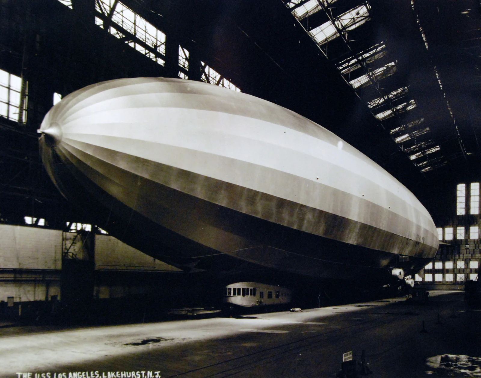 The silver Navy airship USS Los Angeles resting inside a vast hangar at Lakehurst, light streaming through the roof windows