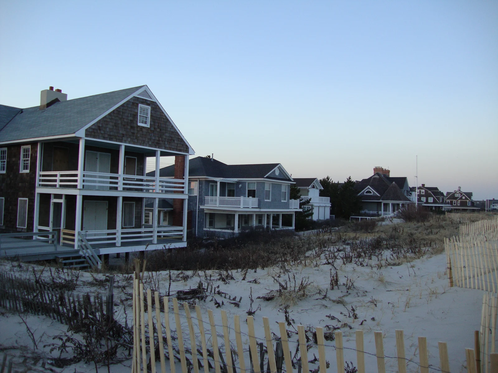 Shingled oceanfront houses with wide porches behind the dunes and sand fencing at Princeton Avenue