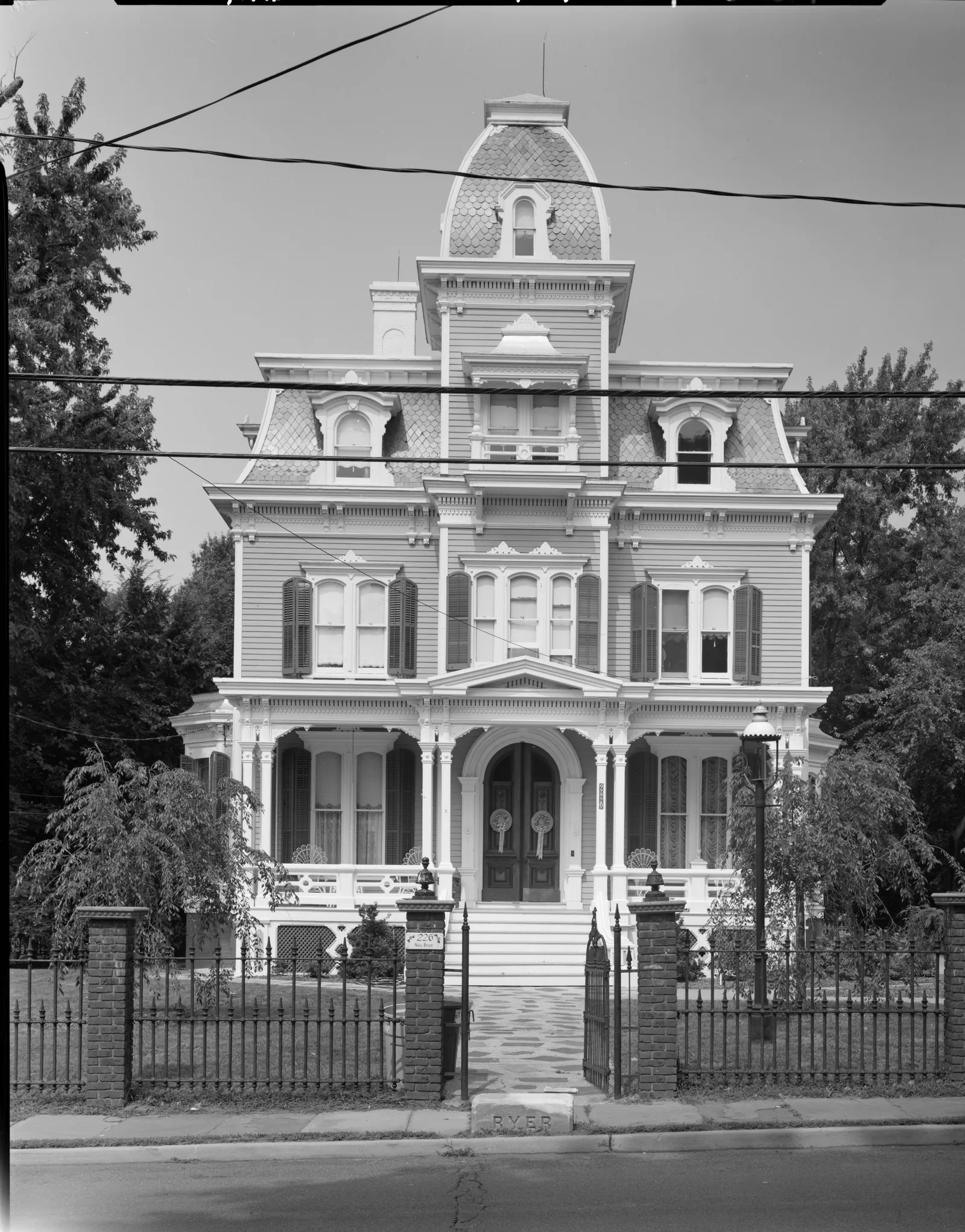 Black and white photo of an ornate Second Empire house with a mansard roof and cupola behind an iron fence at 226 Main Street