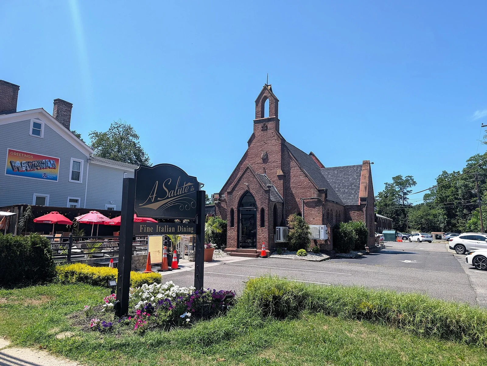 A Salute Italian restaurant in a red brick former church on Main Street, with red umbrellas on the patio and a Greetings from Matawan mural nearby