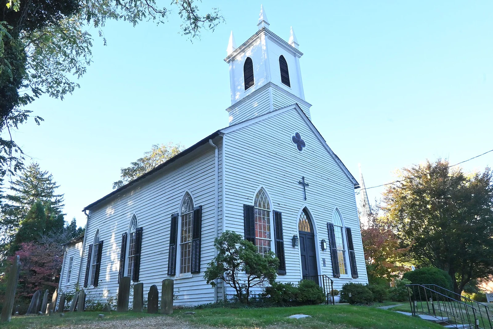 White clapboard Christ Church with a square bell tower and arched windows, with old gravestones on the lawn
