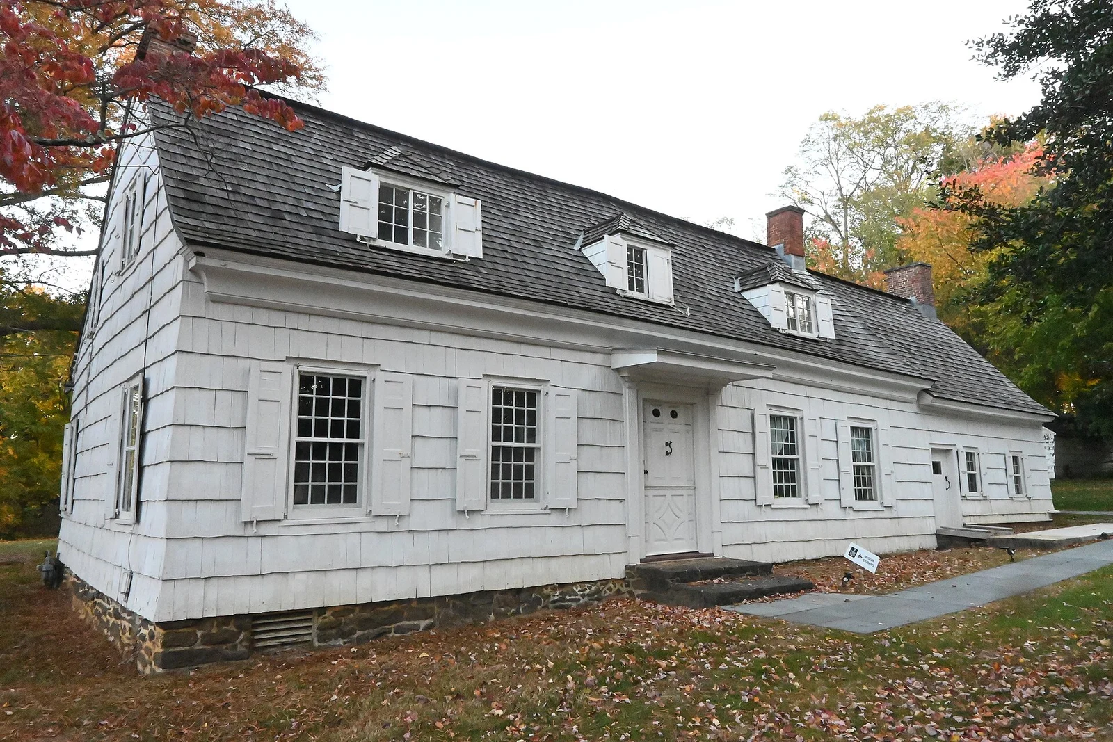 Marlpit Hall, a long white colonial house with a gambrel roof and dormers, framed by autumn trees on Kings Highway