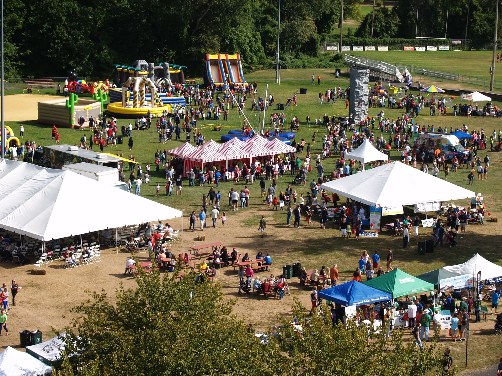 Crowds filling a big lawn between white tents, striped vendor booths and inflatable slides at the Middletown Day festival, seen from above