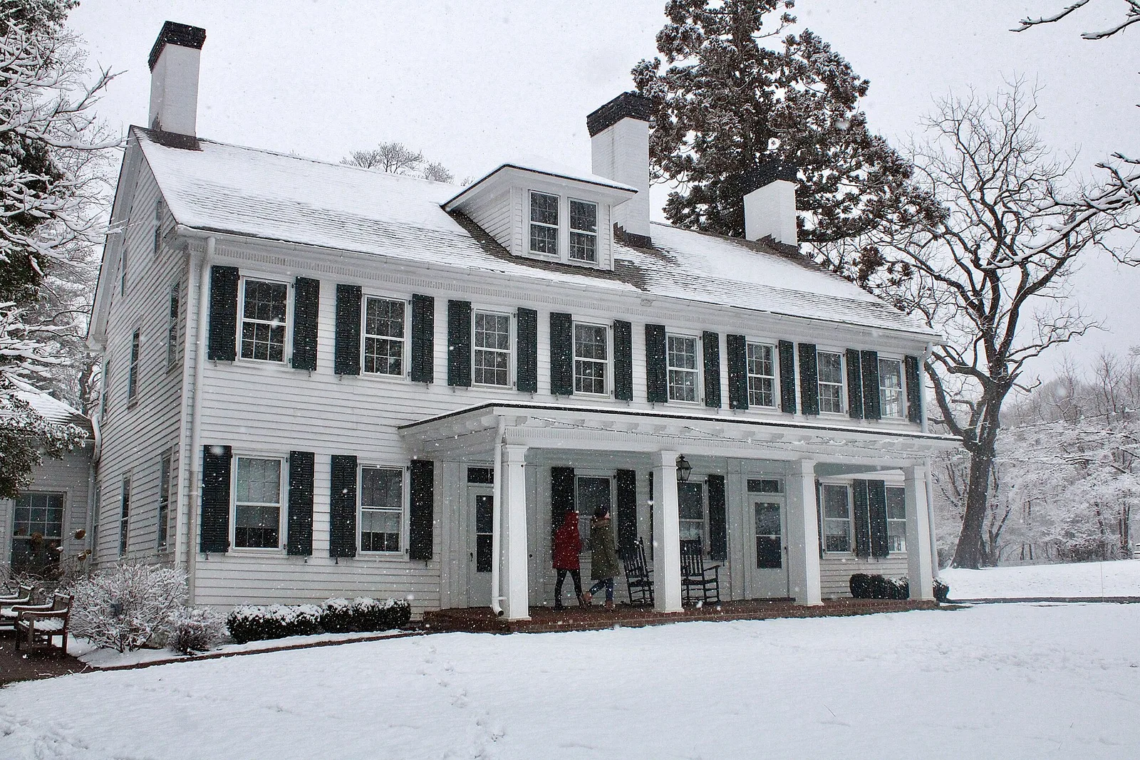 The white Tatum homestead with black shutters and a front porch under fresh snow at Tatum Park