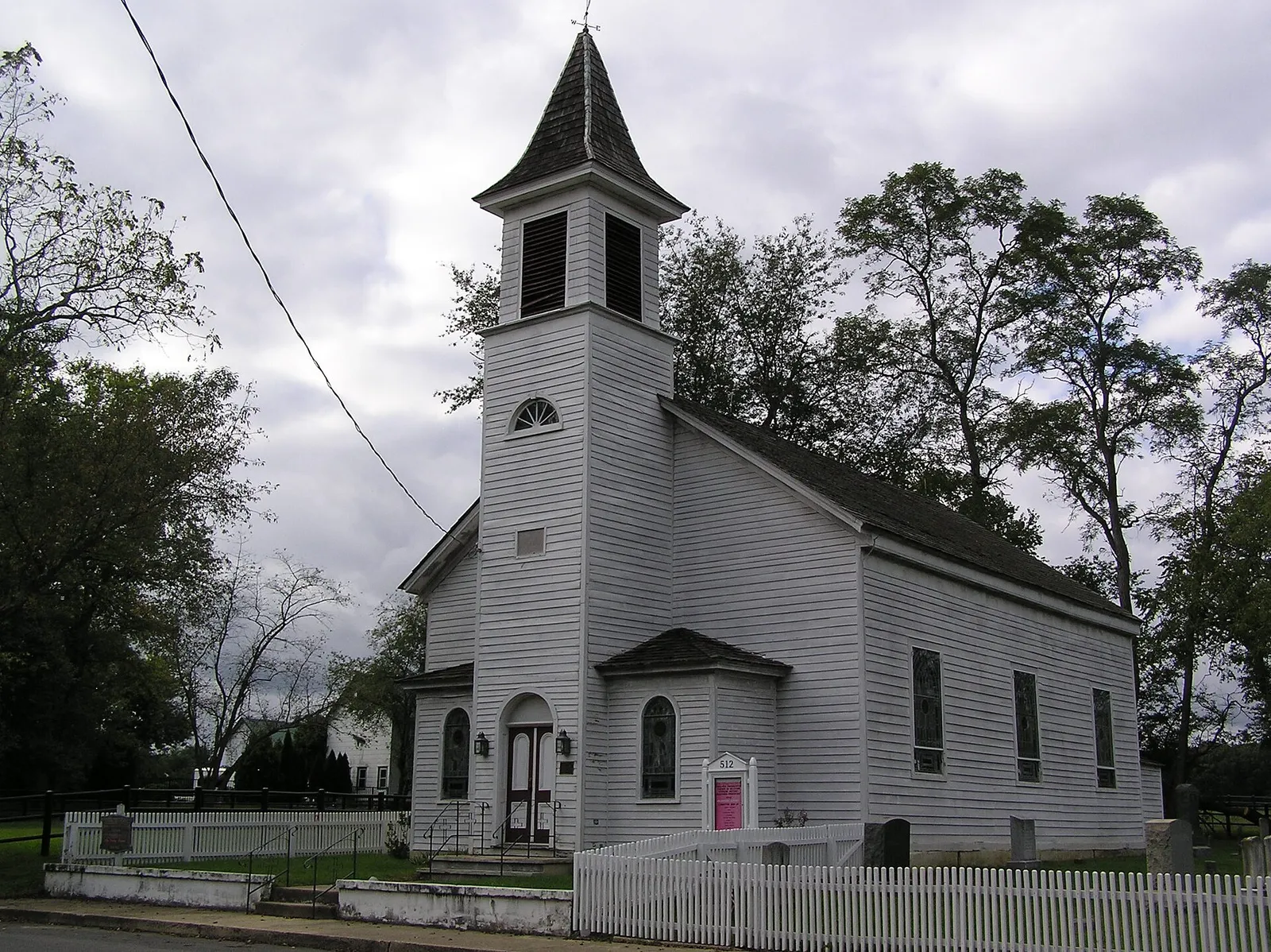 White clapboard church with a tall steeple and a picket fence under a cloudy sky