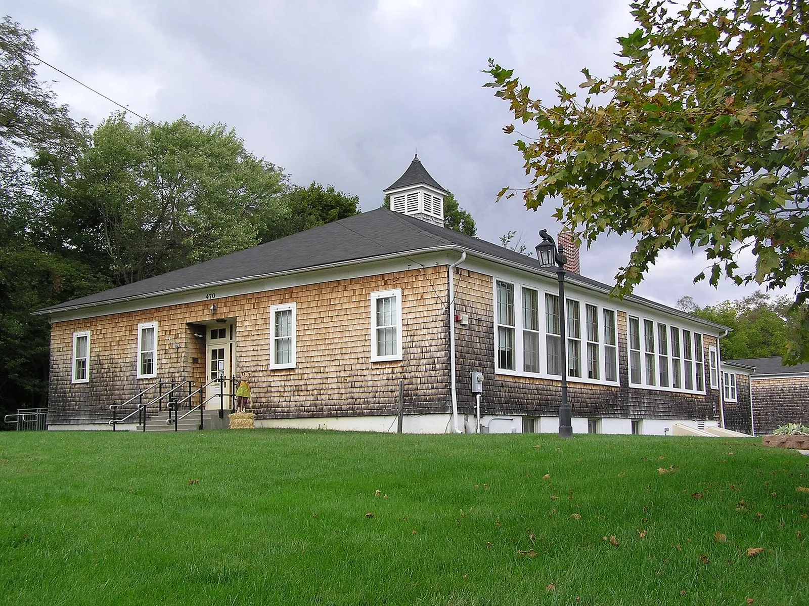 Long cedar-shingled schoolhouse with a cupola on a green lawn