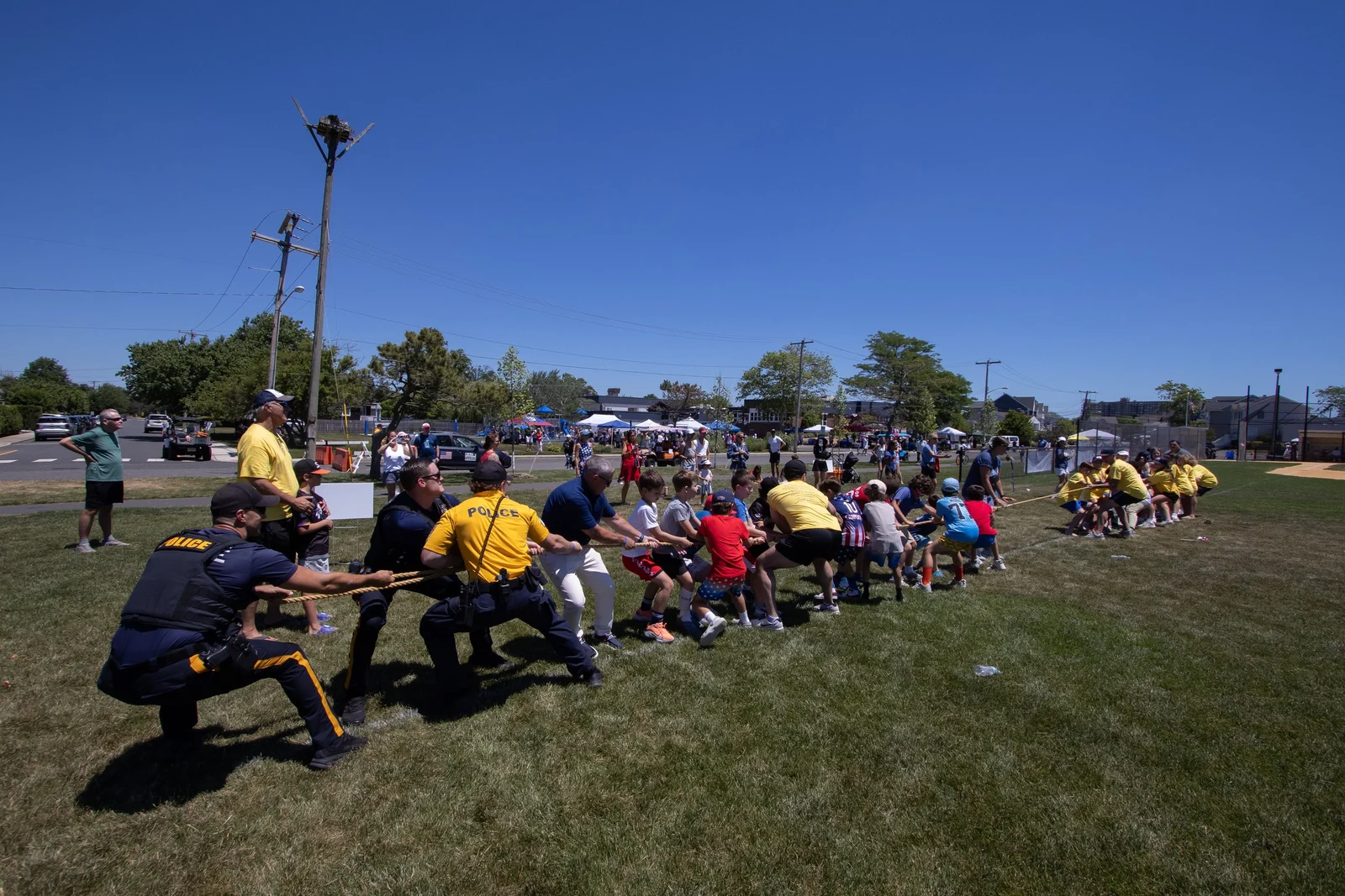 Teams pull hard on a long rope in a tug of war on a grassy field during the America 250 field day, with spectators behind