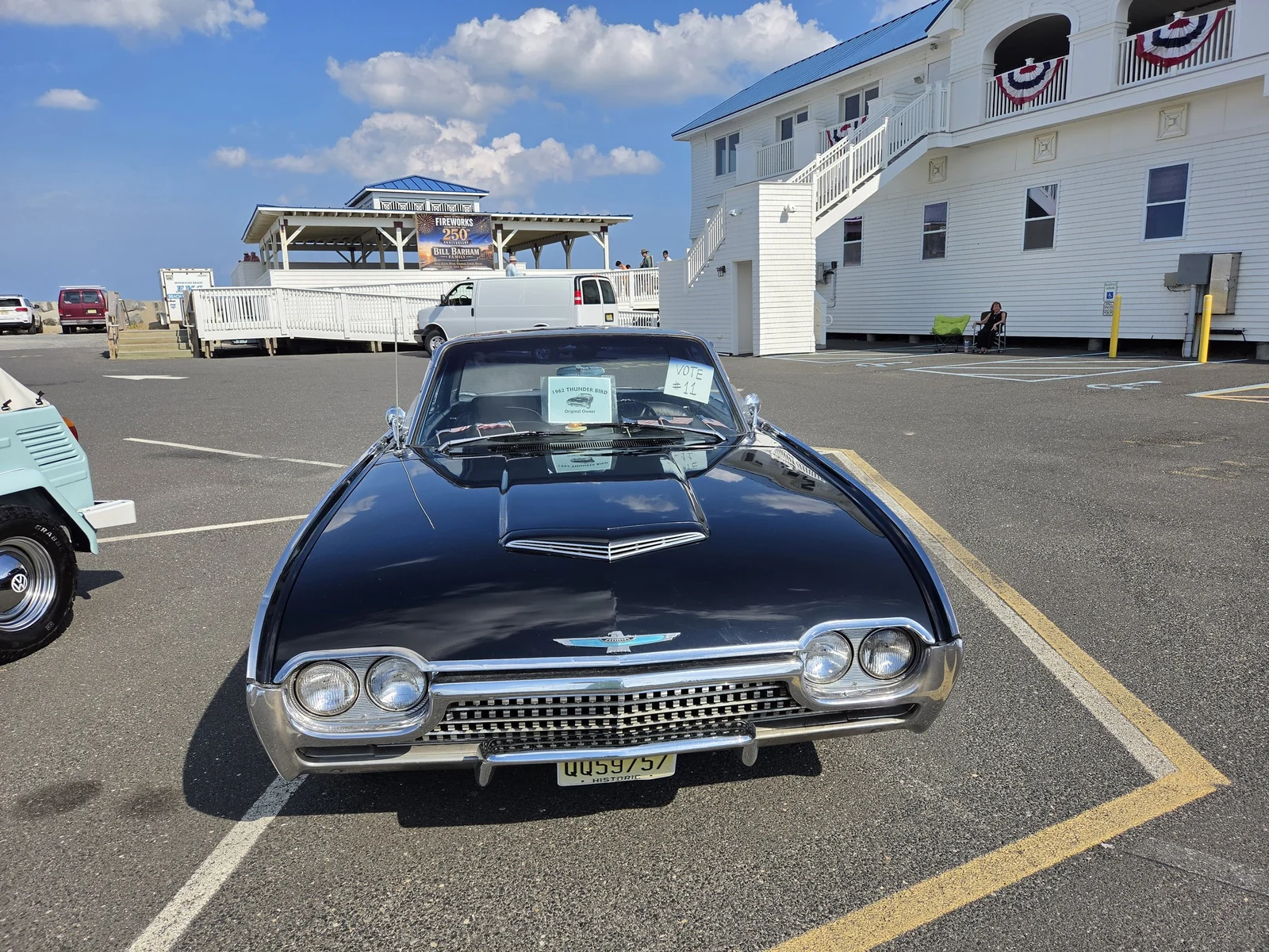 A shiny black classic car parked for the antique car show beside the bunting-draped Bathing Pavilion