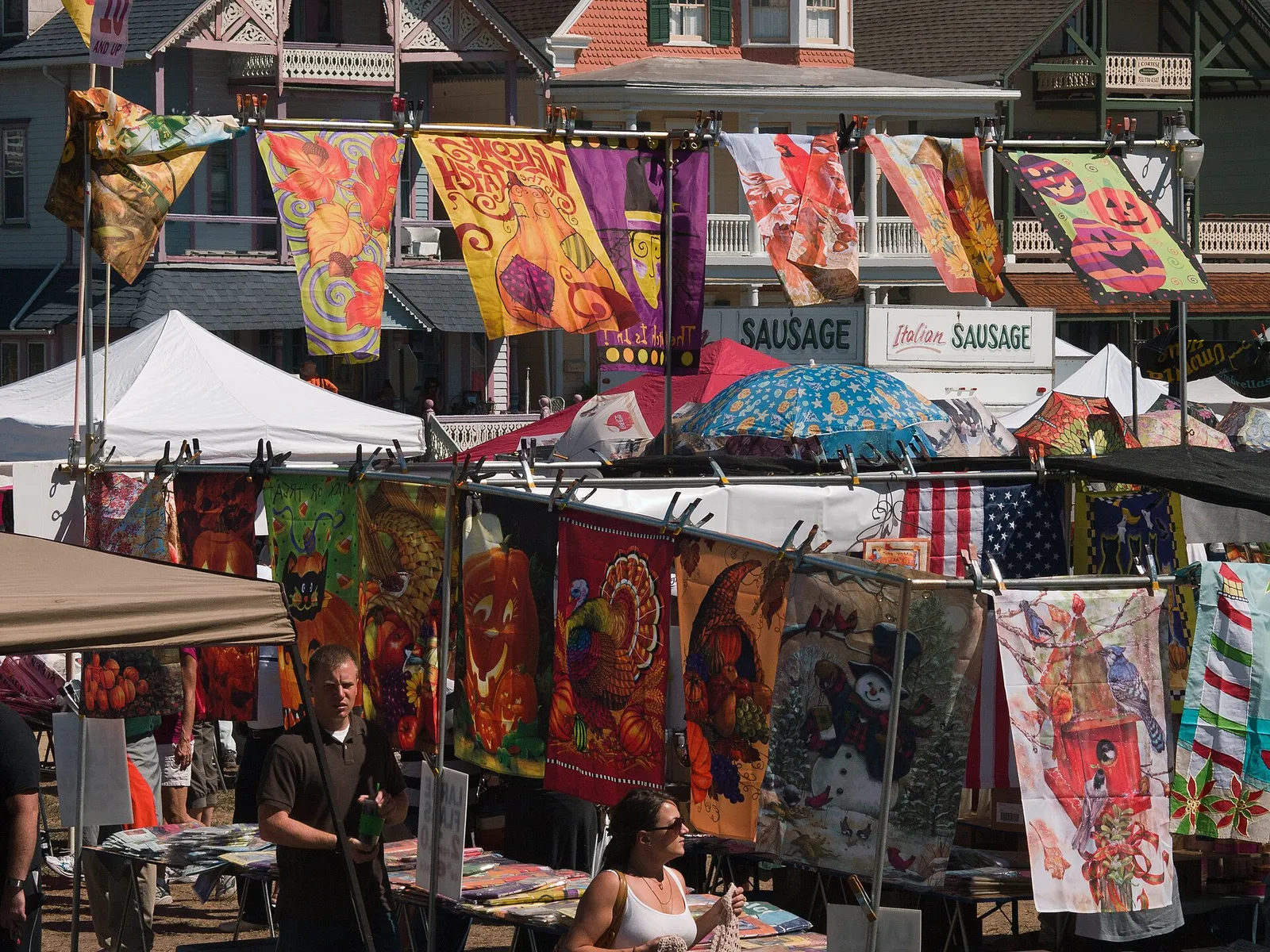 Rows of colorful decorative flags hanging above vendor tents in front of Victorian buildings