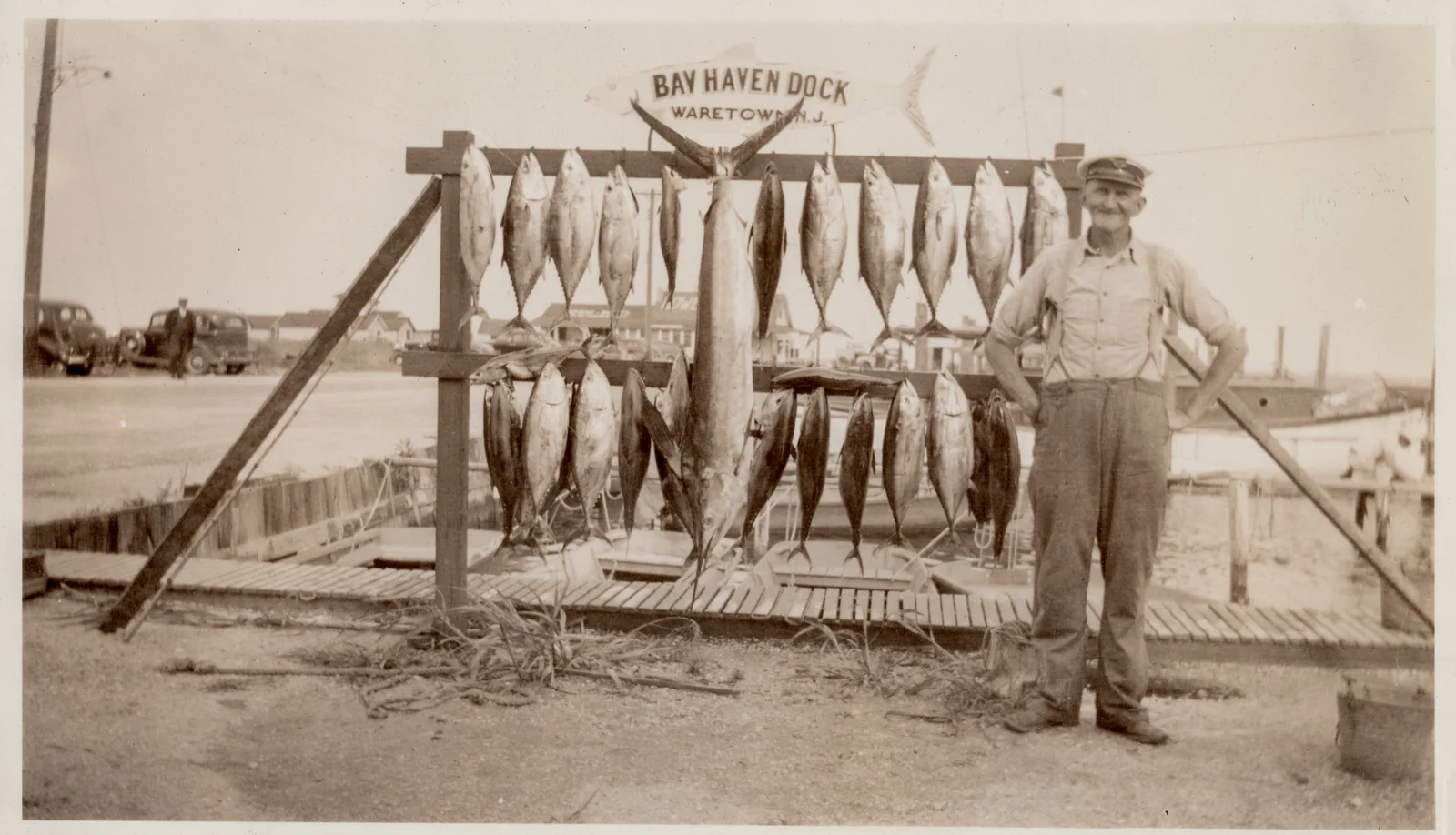 Vintage photo of an angler in a cap and suspenders beside a rack of tuna and a large marlin under a Bay Haven Dock, Waretown sign