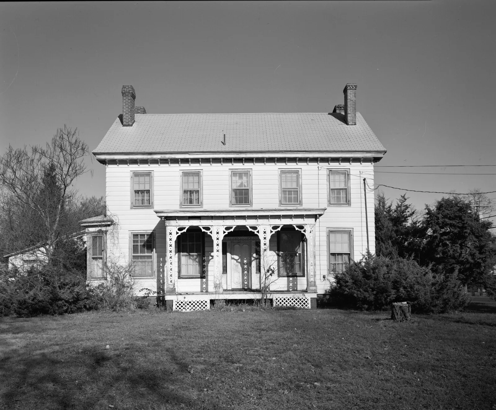 A two-story historic house with a decorative front porch and twin chimneys, in black and white