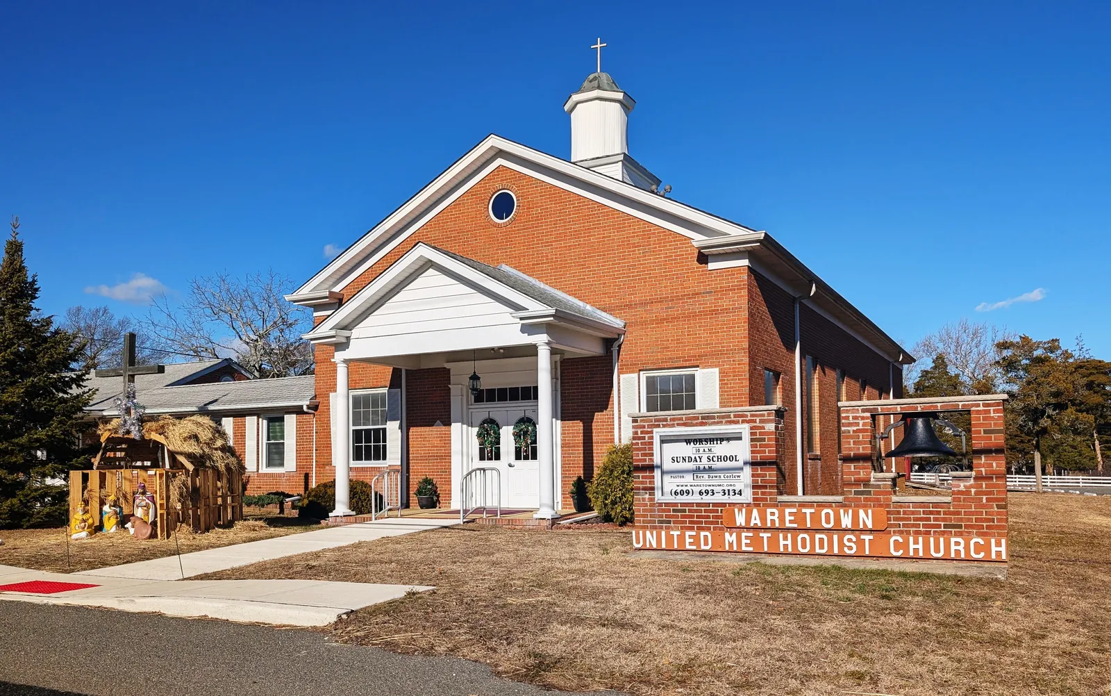A red brick church with a white columned portico and cupola under a clear blue sky