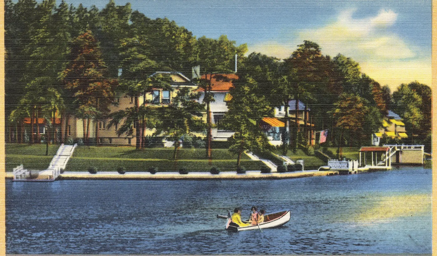 Vintage tinted postcard of houses among tall trees along the shore of Deal Lake, with a small rowboat on the water