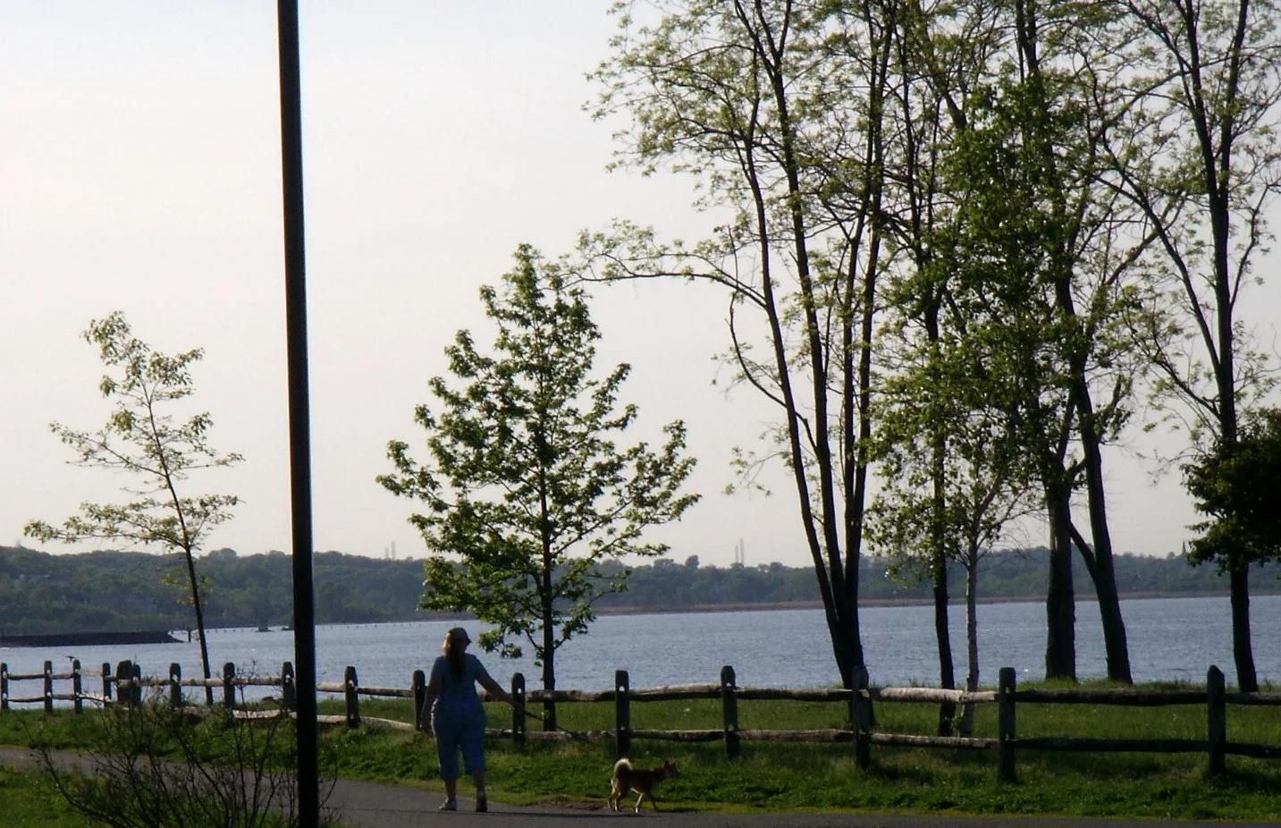A wooden boardwalk with railings and lampposts running along the Raritan Bay shore at Old Bridge Waterfront Park in Laurence Harbor