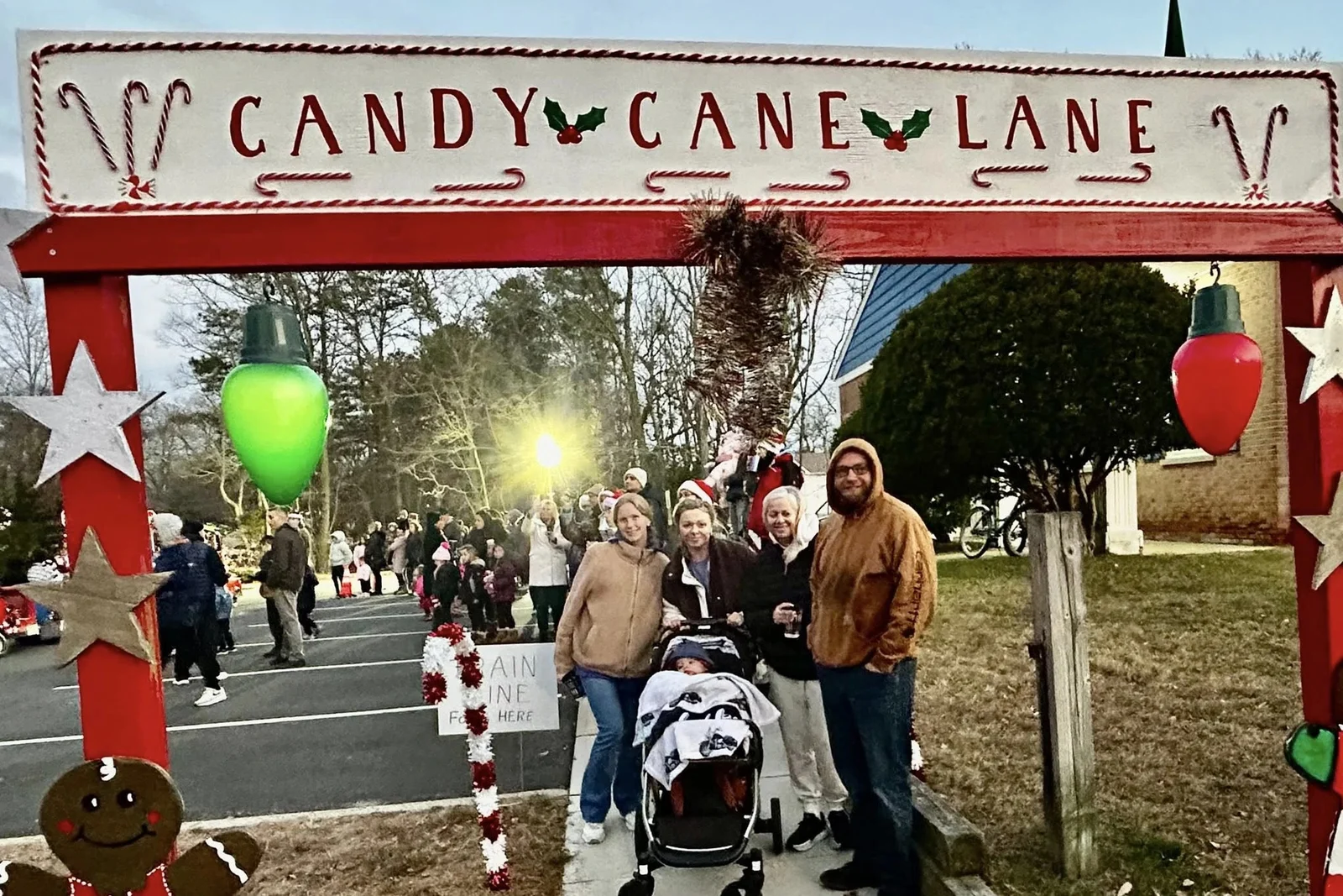 Visitors walking under a red Candy Cane Lane arch decorated with giant string lights, stars and a gingerbread figure at a Pine Beach holiday event