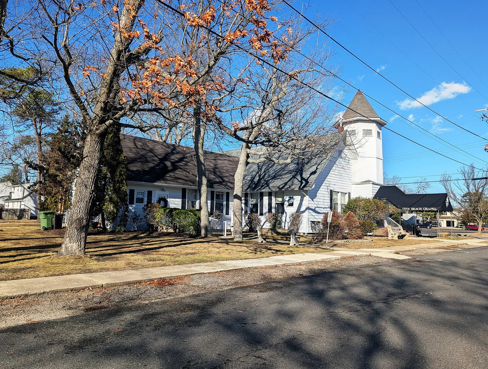 A white chapel with a pointed bell tower behind autumn trees under a blue sky