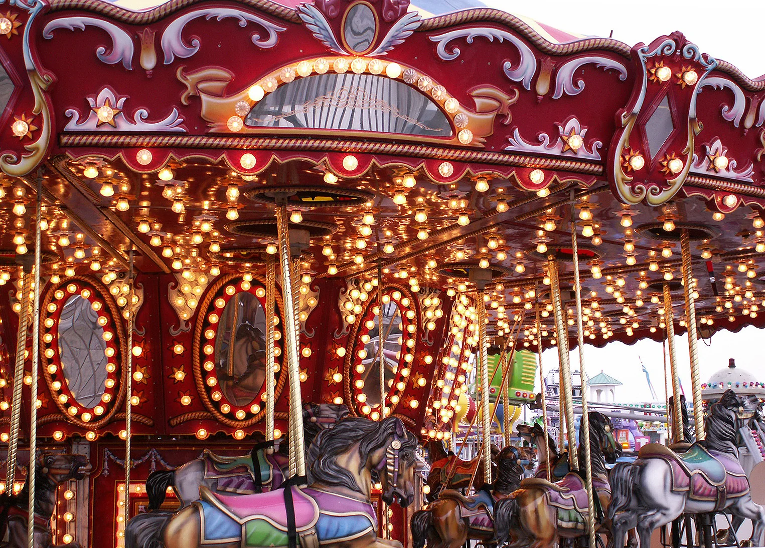 A red and gold merry-go-round glowing with hundreds of lights, its painted horses in the foreground