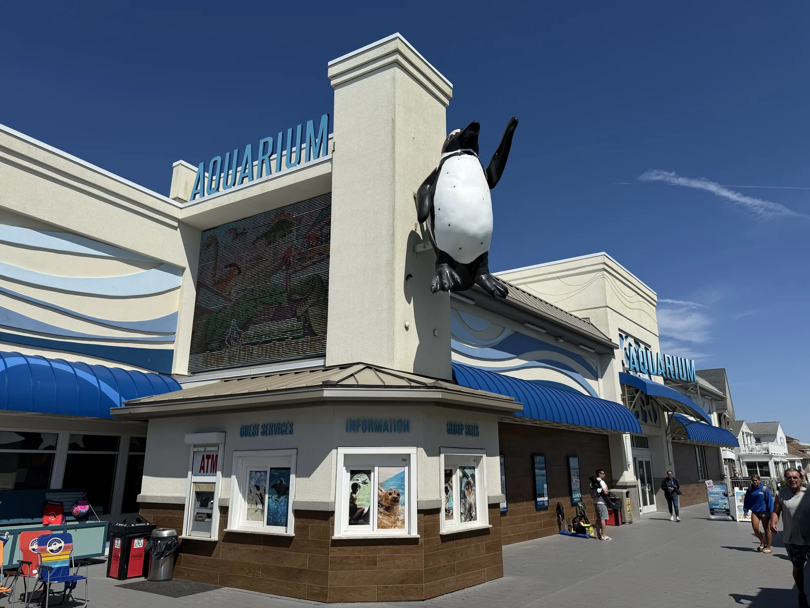 The white boardwalk entrance of Jenkinson's Aquarium with blue awnings and a large penguin statue on its tower