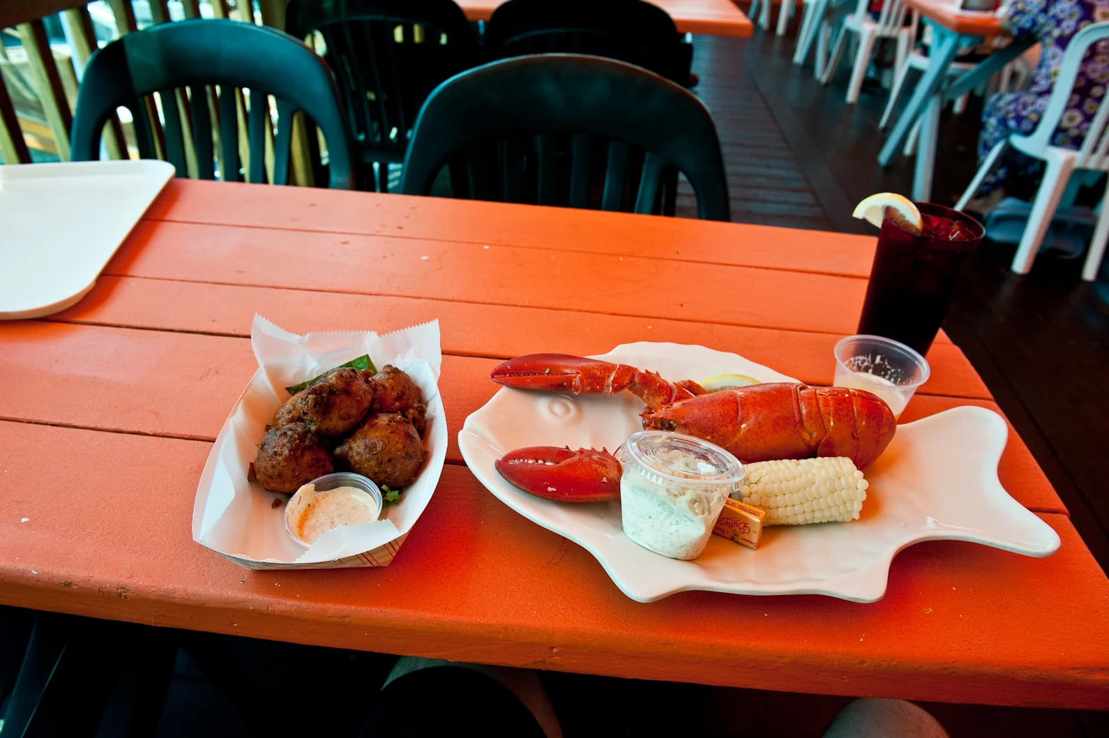 A whole lobster with corn on the cob and lobster and corn fritters on an orange picnic table at Red's Lobster Pot