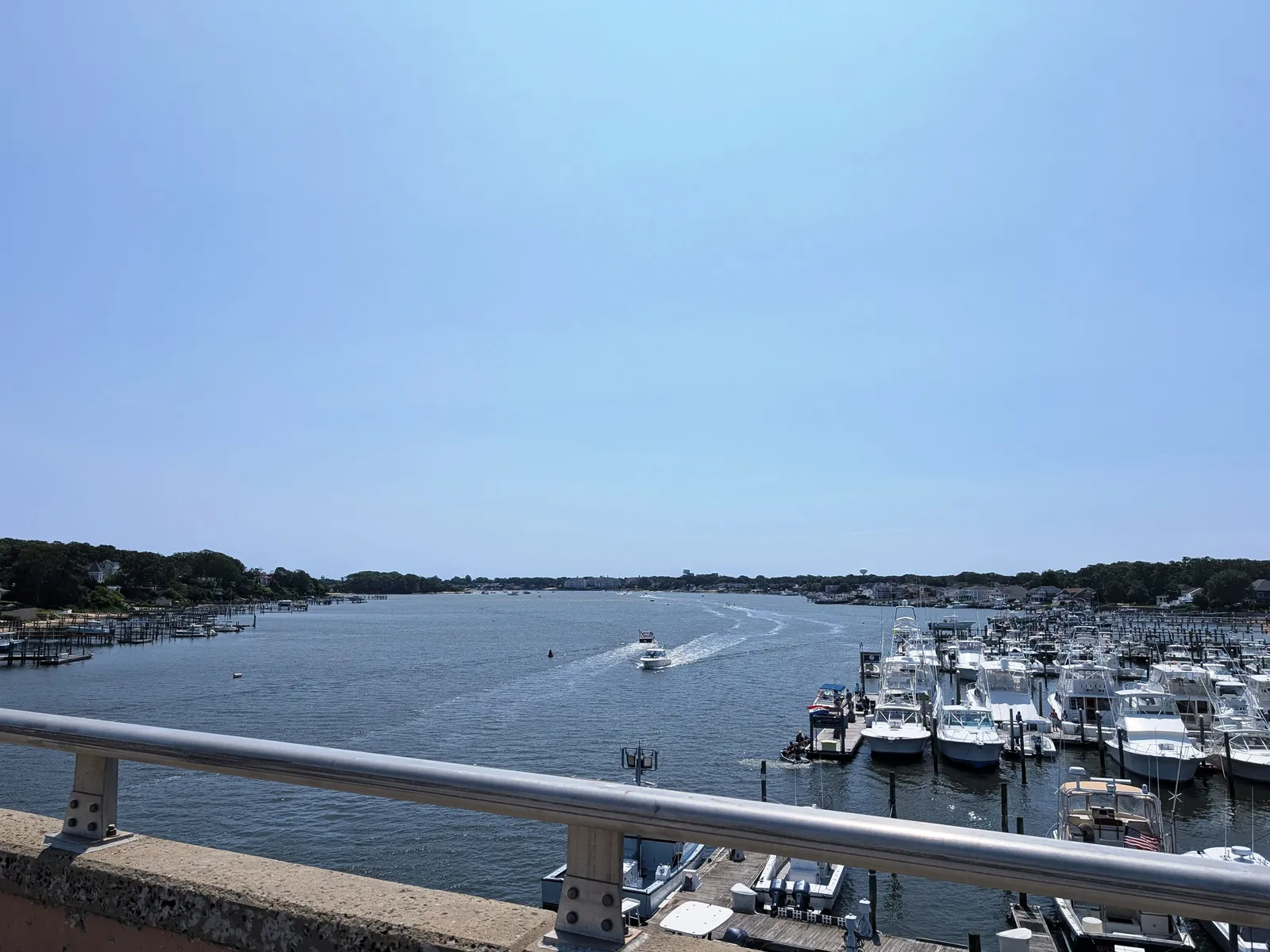 The Manasquan River under a clear sky, with boats docked at marinas along the right bank