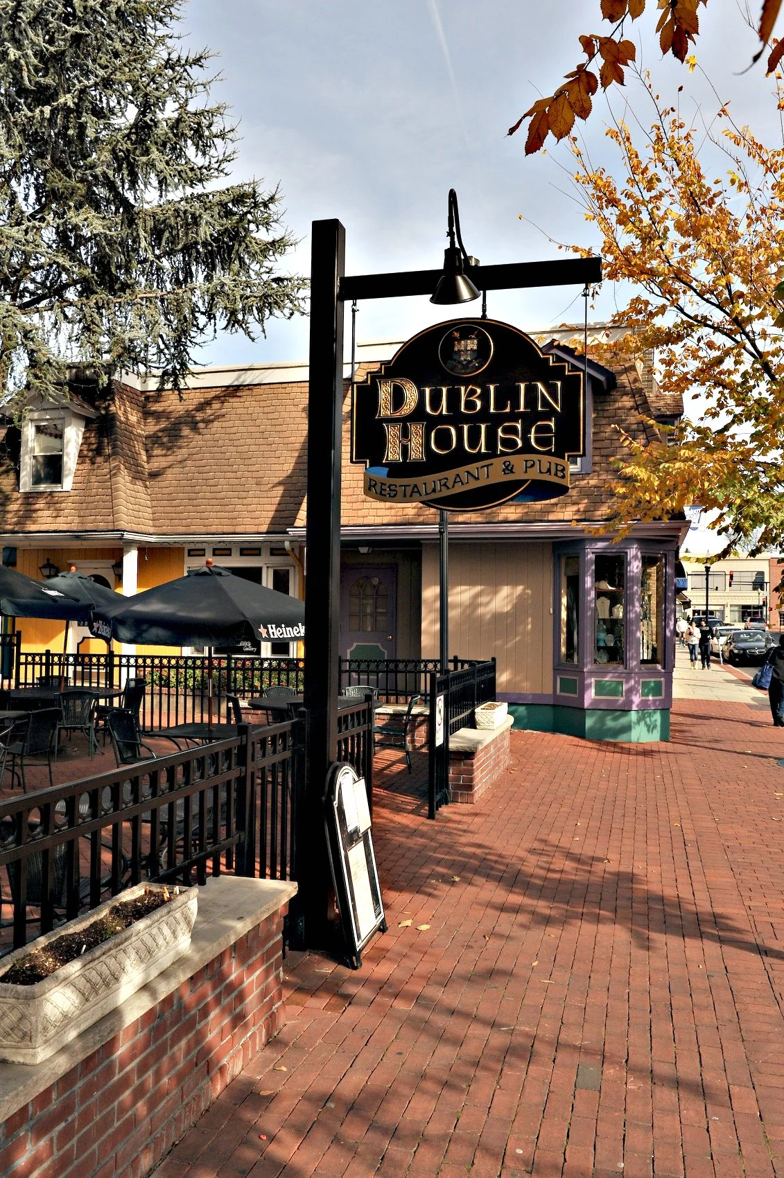 The hanging sign of the Dublin House Restaurant & Pub above a brick walkway and outdoor patio in autumn