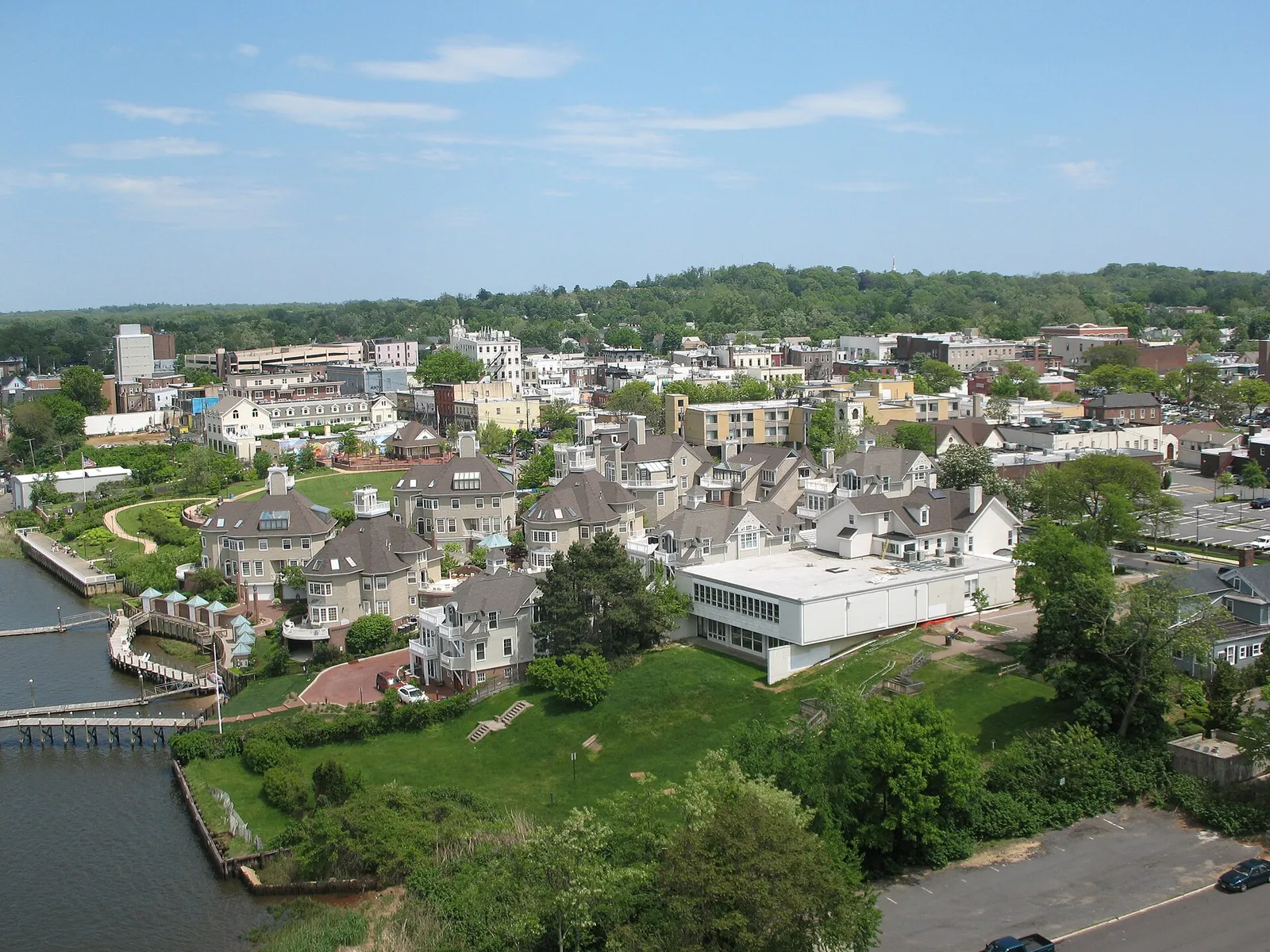 Aerial view of a riverside town of shingled buildings, green lawns and a waterfront path beside the river