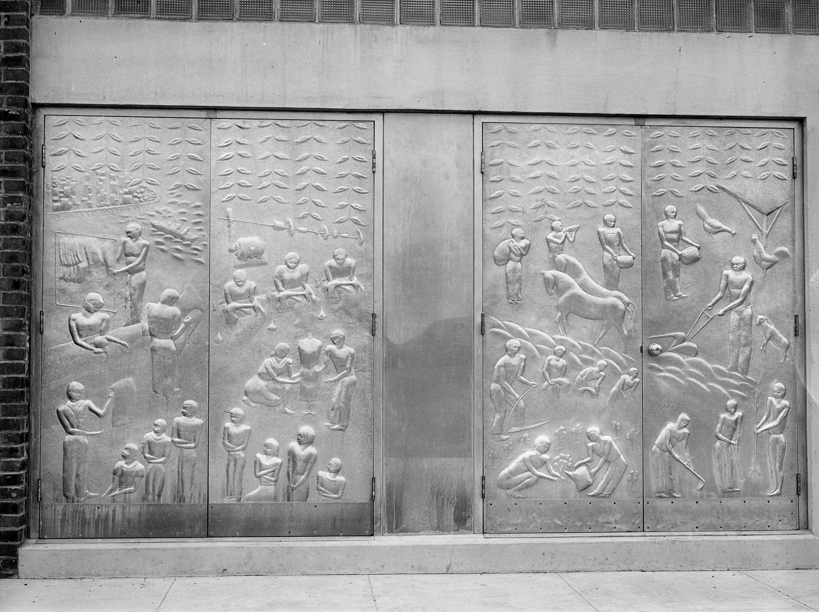 A pair of aluminum entrance doors covered in relief panels of figures at work, at the Jersey Homesteads community building