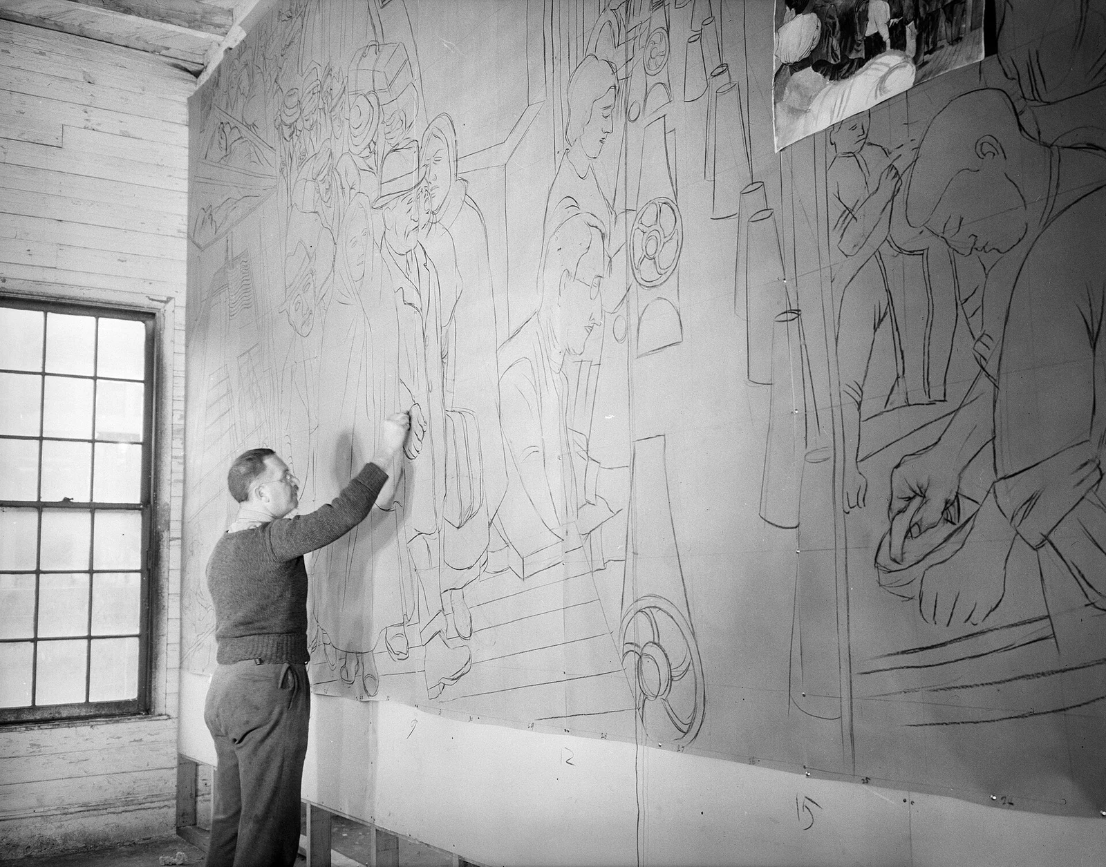 A man drawing the outlines of the Ben Shahn mural in charcoal on a long wall beside a window, 1938