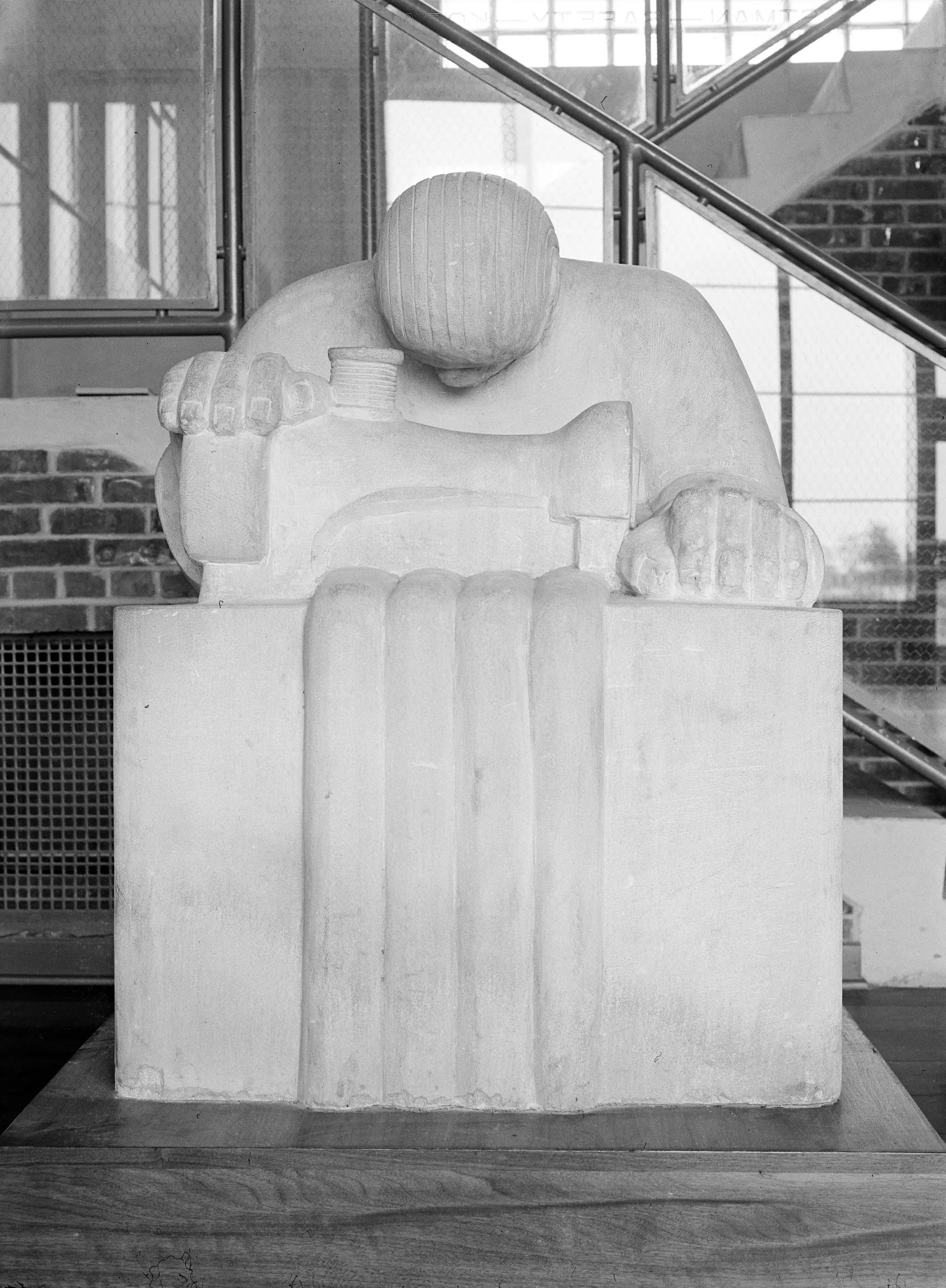 A white limestone sculpture of a seated garment worker bent over her work, beside a stairway in the community building