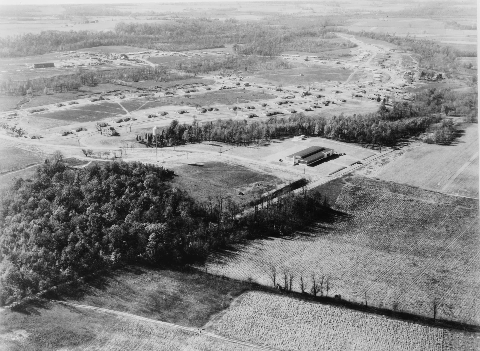 Black and white 1938 aerial photo of Jersey Homesteads, with rows of new flat-roofed houses and the cooperative factory among woods and farm fields