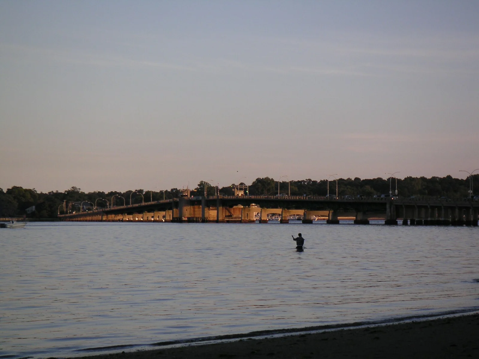 Calm Navesink River at dusk with the long Oceanic Bridge on the far shore and a lone angler wading