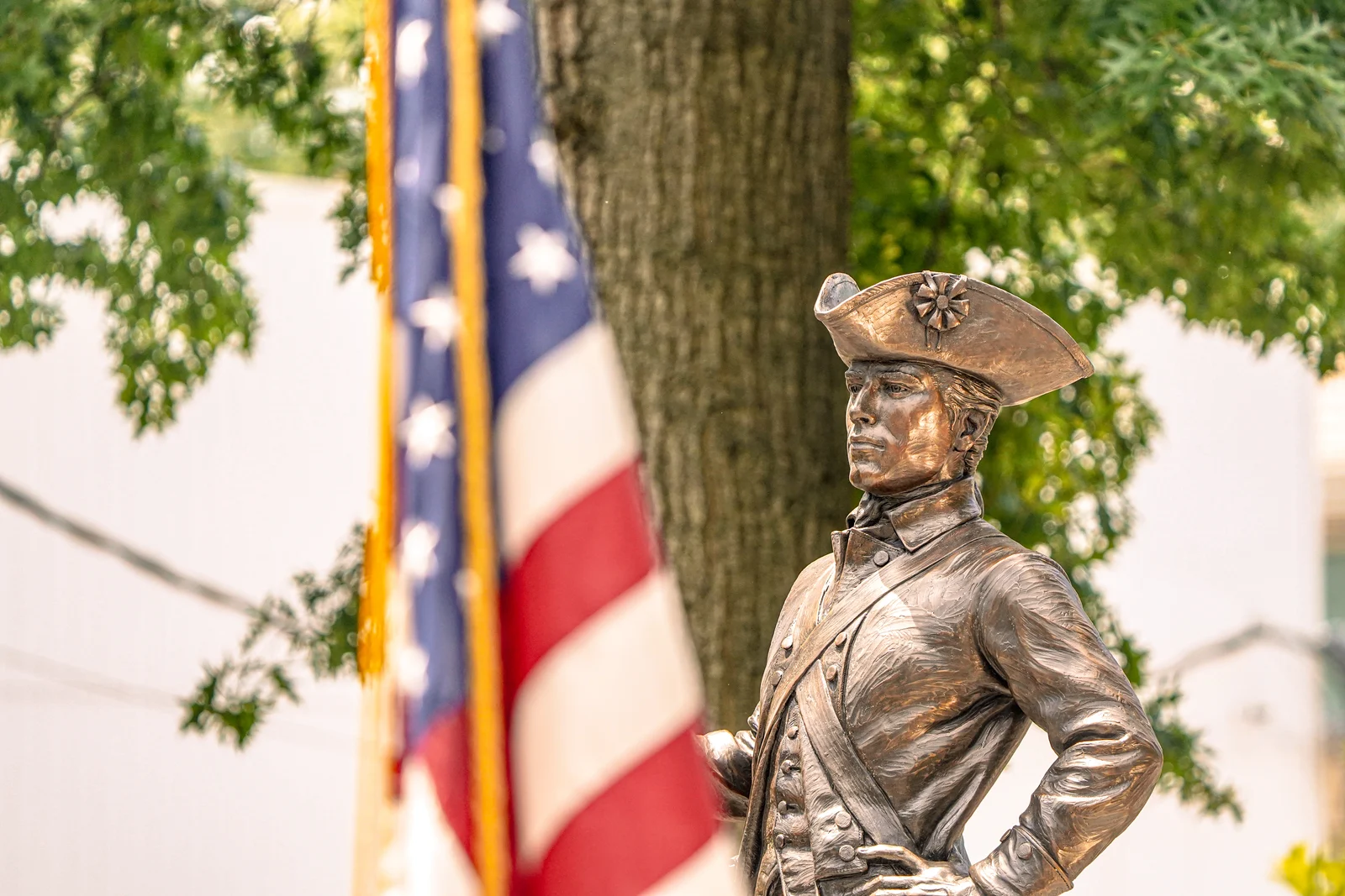 Bronze statue of a Revolutionary War soldier in a tricorn hat beside an American flag in Victory Park