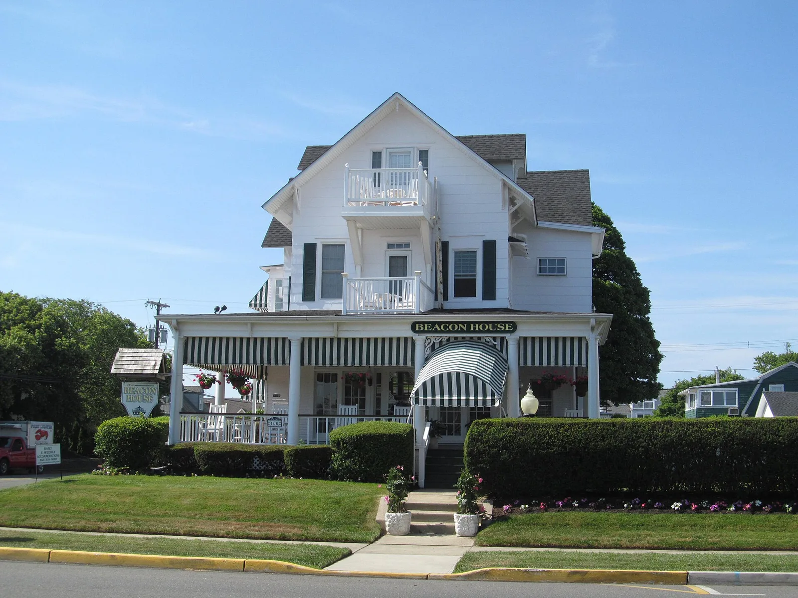 The white Beacon House in Sea Girt with striped awnings, balconies and a clipped hedge in front