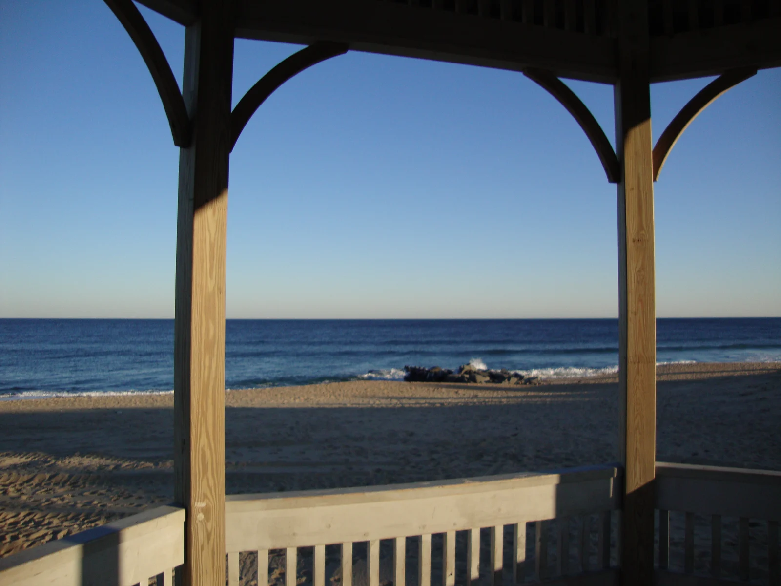 The ocean and an empty winter beach framed by the wooden posts and railing of a gazebo