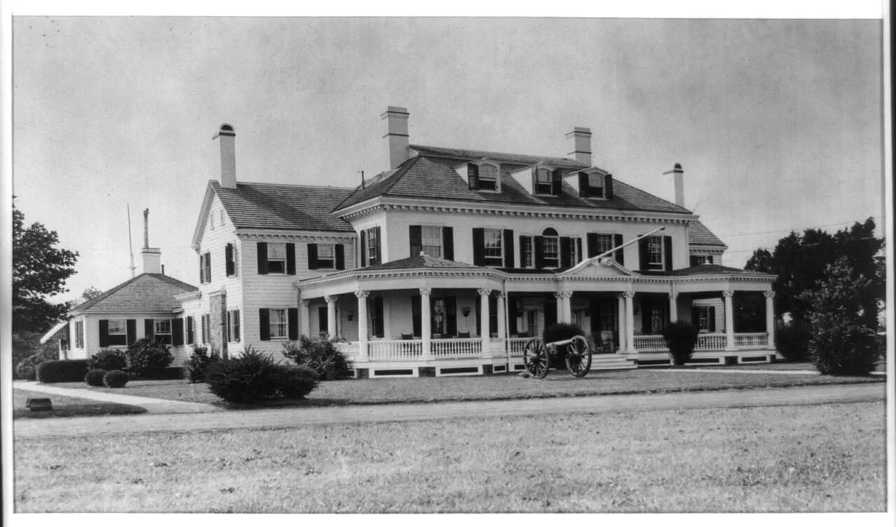 Black and white 1912 photo of the governor's summer mansion at Sea Girt, a large white house with porches and a cannon on the lawn