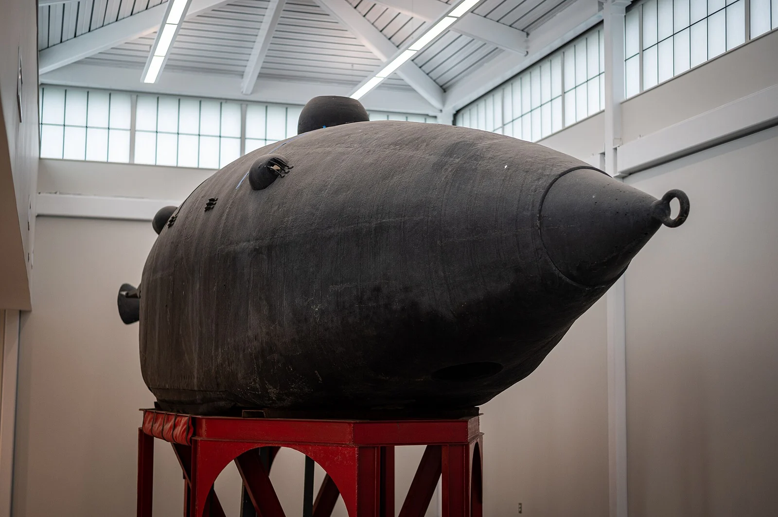 The Intelligent Whale, a dark iron hand-cranked submarine shaped like a blunt torpedo, on a red steel stand in a bright museum hall