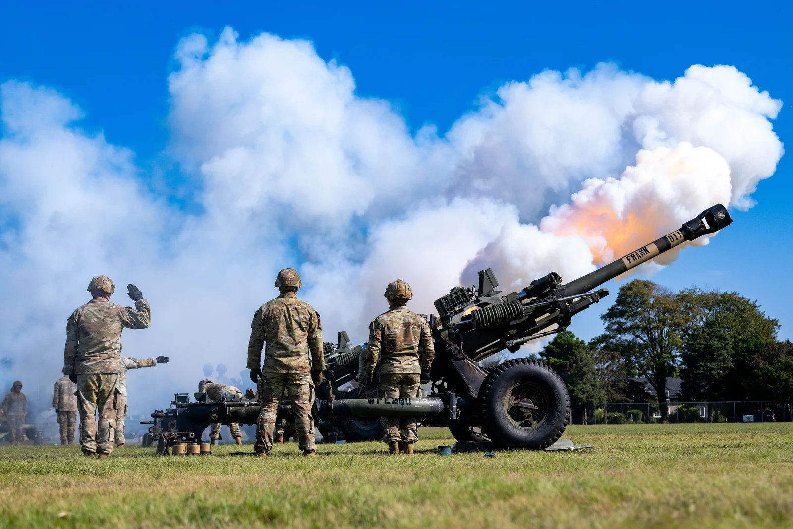 New Jersey Army National Guard soldiers saluting as M119A3 howitzers fire a salute in a cloud of white smoke on the parade field