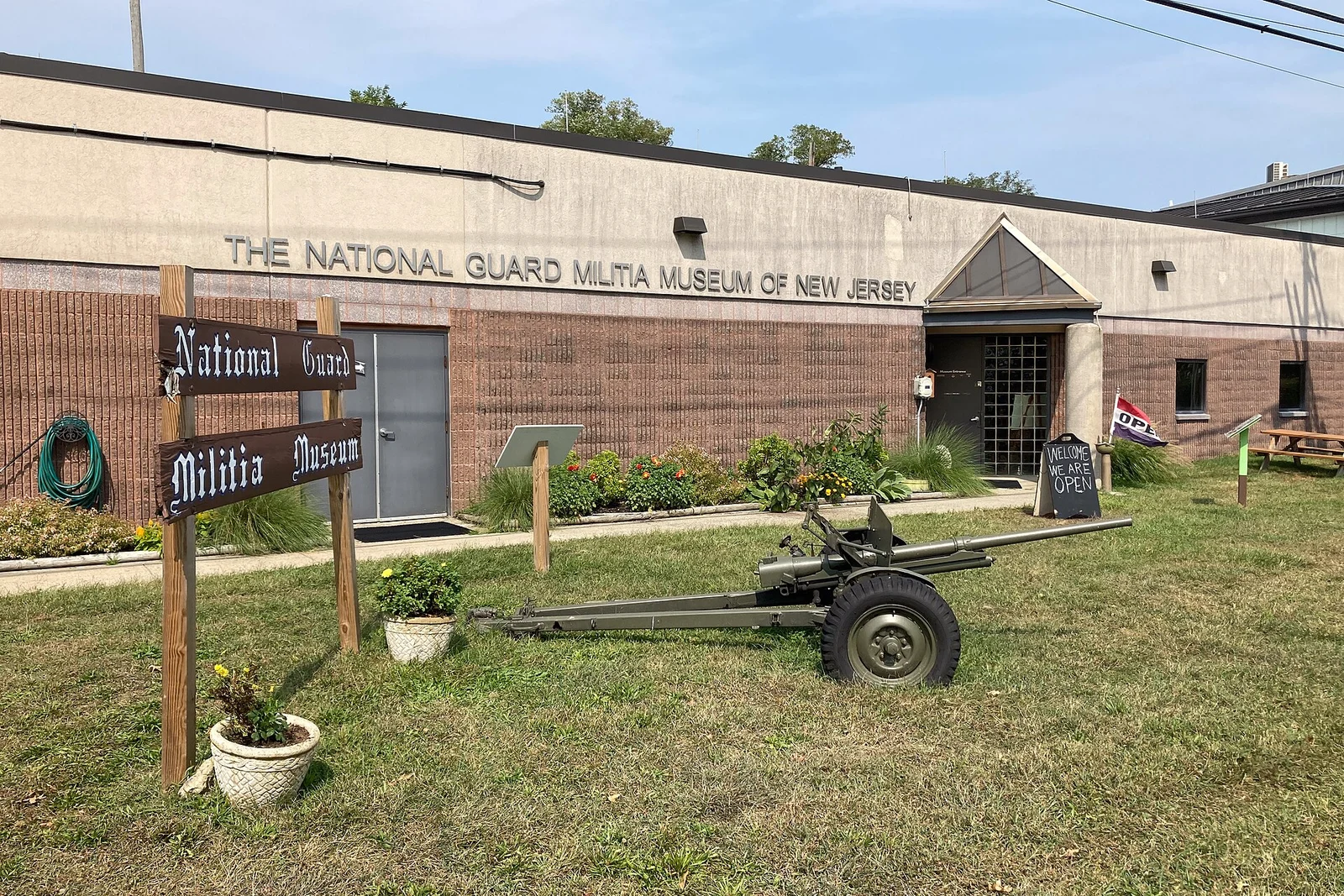Brick front of the National Guard Militia Museum of New Jersey with a wooden sign and a field gun on the lawn