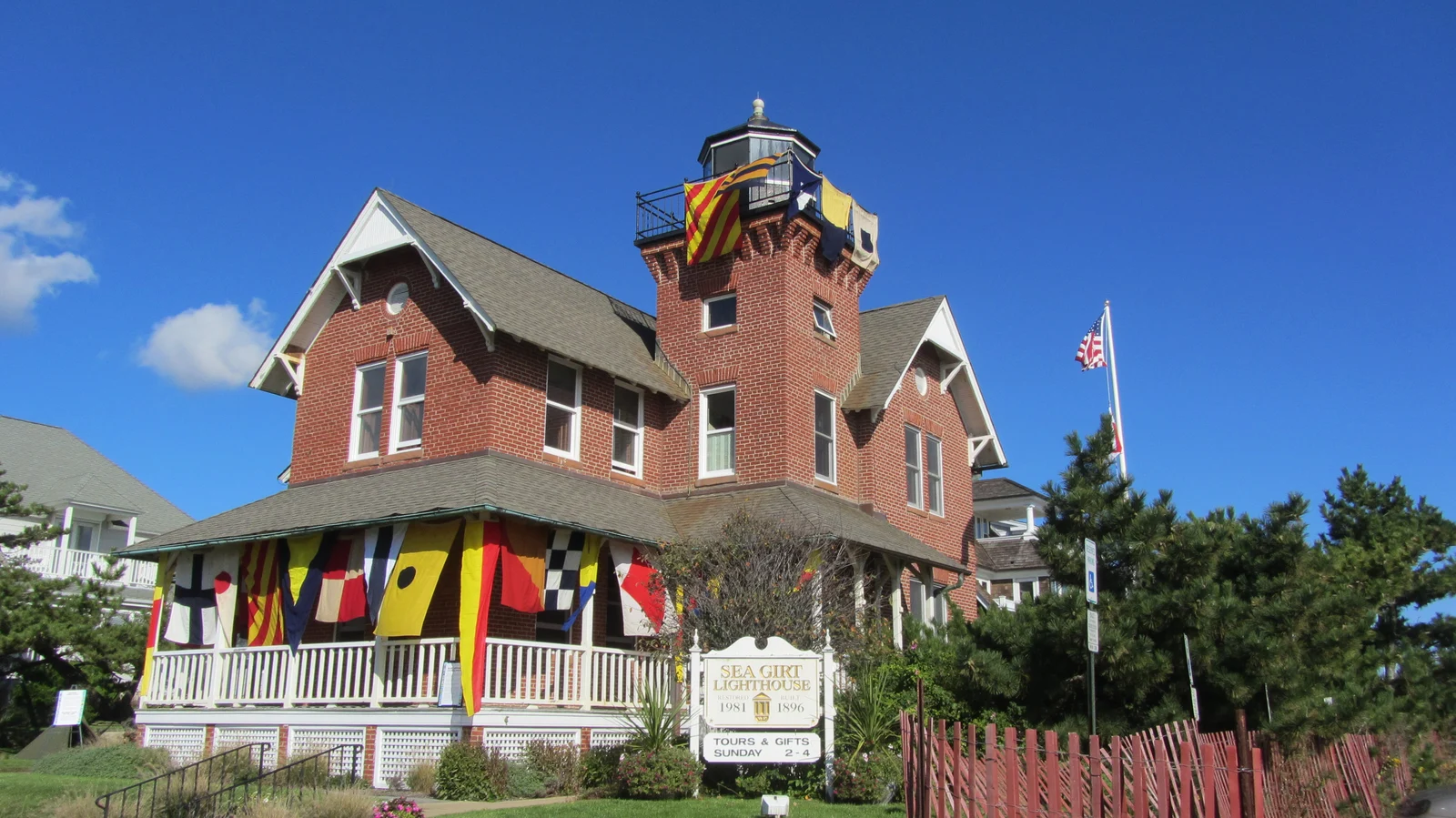 The red brick Sea Girt Lighthouse with colorful nautical signal flags hung across its porch and tower under a deep blue sky