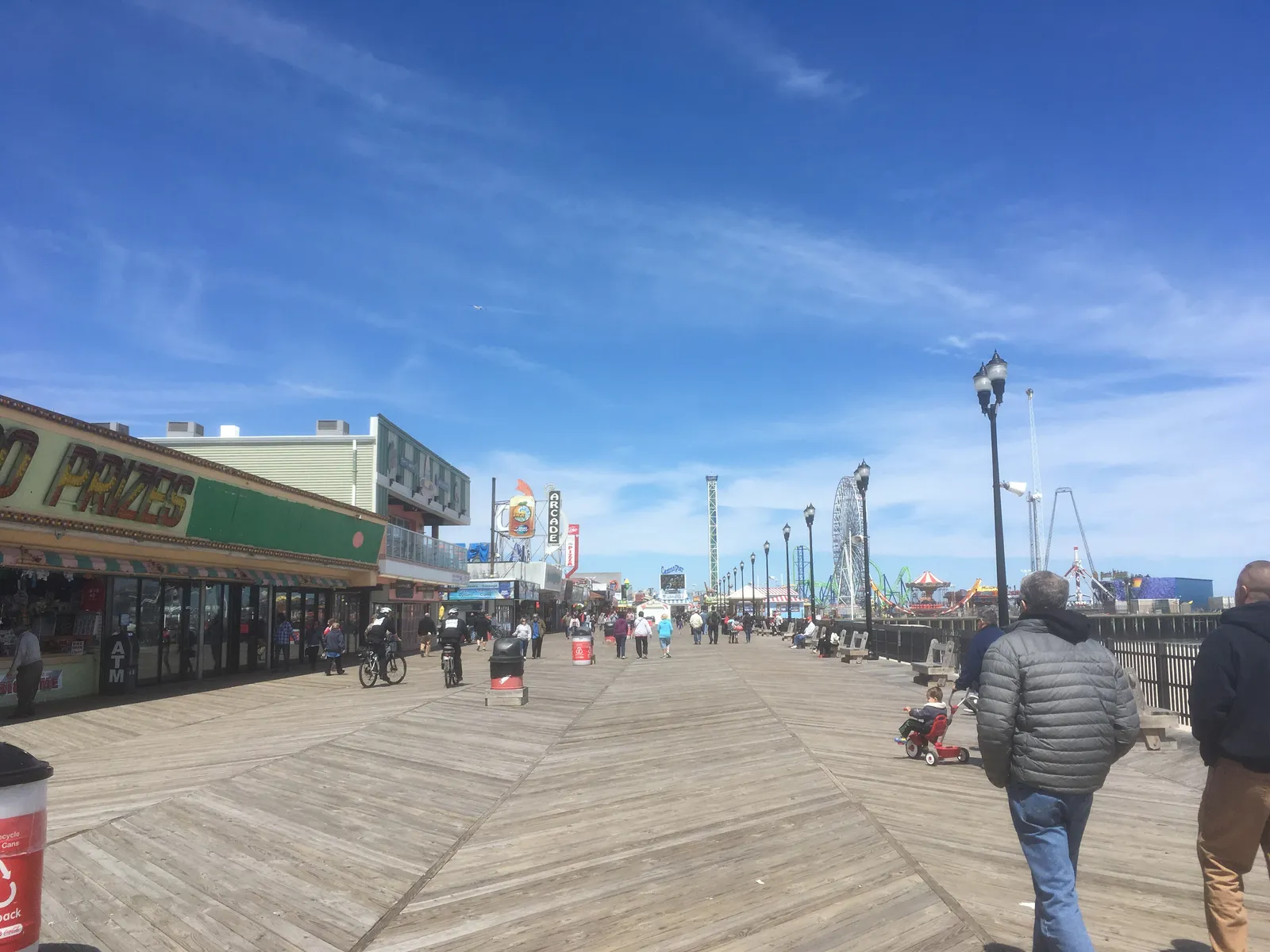 Wide wooden boardwalk lined with shops and lampposts under a blue sky