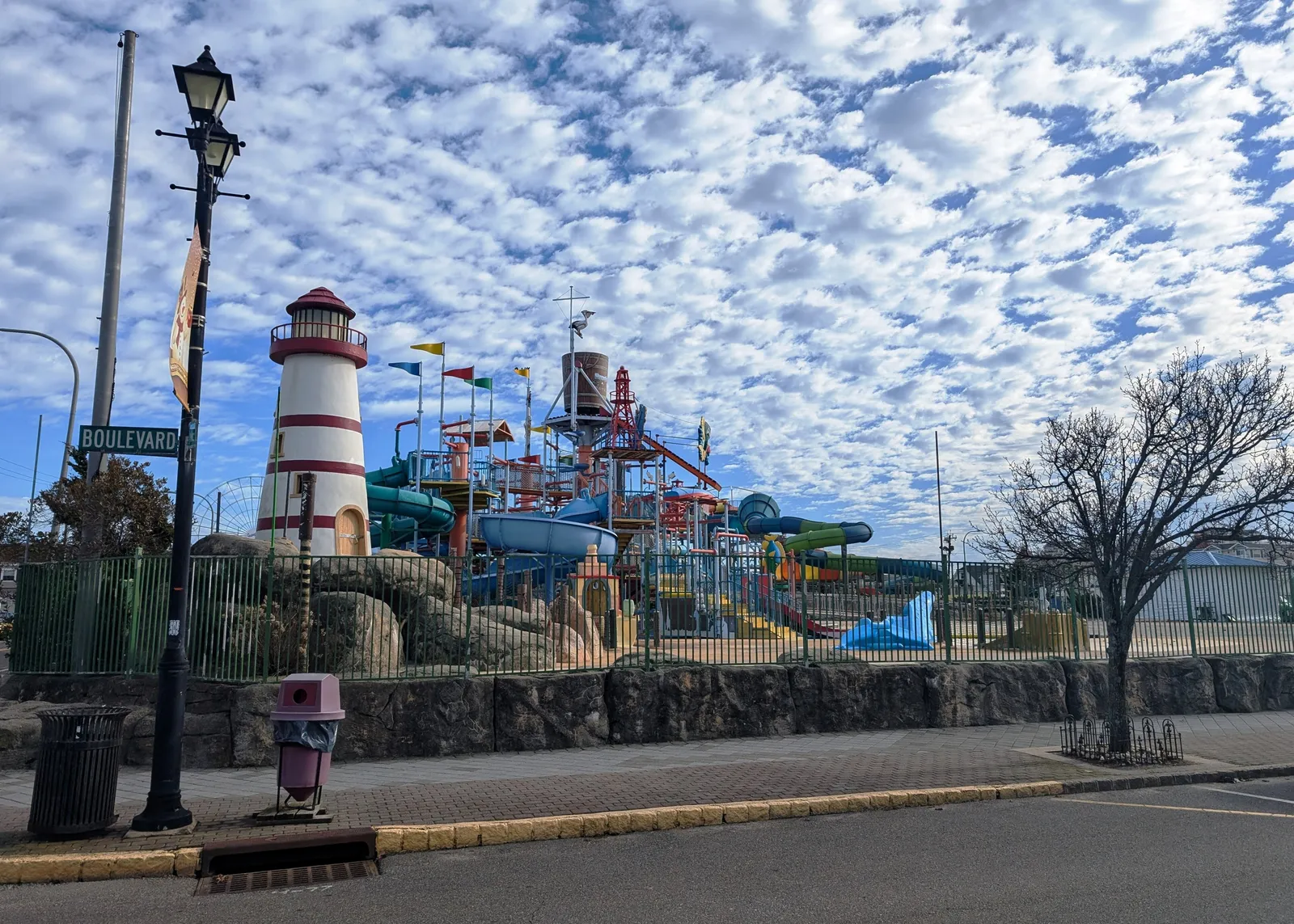 Water slides and a lighthouse tower at the Breakwater Beach waterpark under a cloudy blue sky