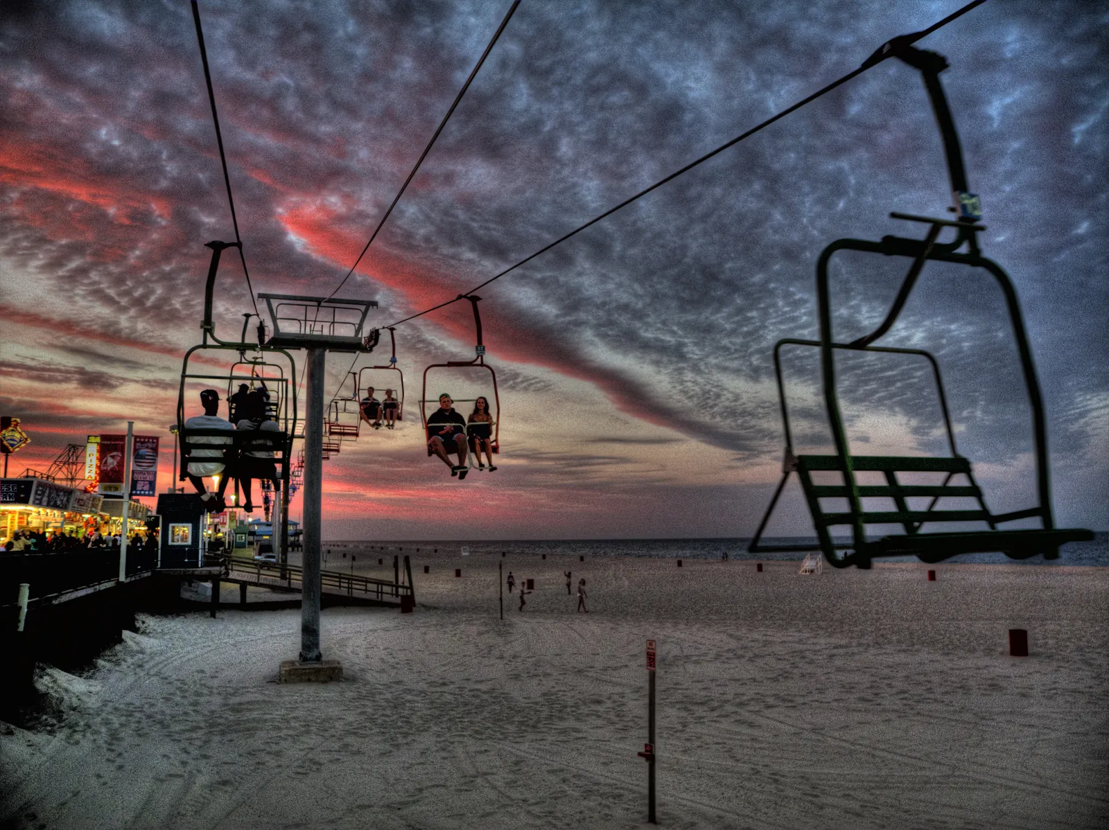 Sky ride chairs crossing above the sand at sunset beside the boardwalk