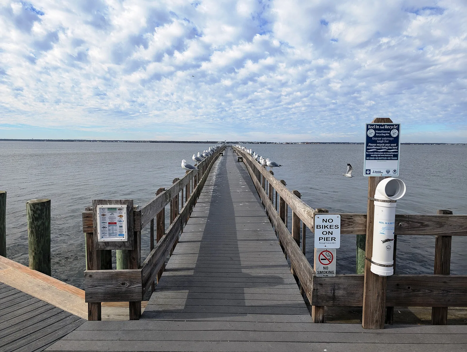 A long wooden fishing pier stretching into Barnegat Bay under a sky of scattered clouds