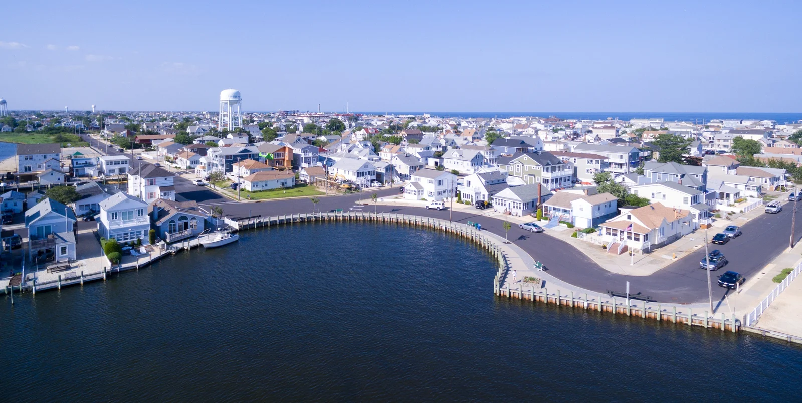 Aerial view of Seaside Park's bayfront homes along a curving bulkheaded lagoon, with the water tower and the ocean on the horizon