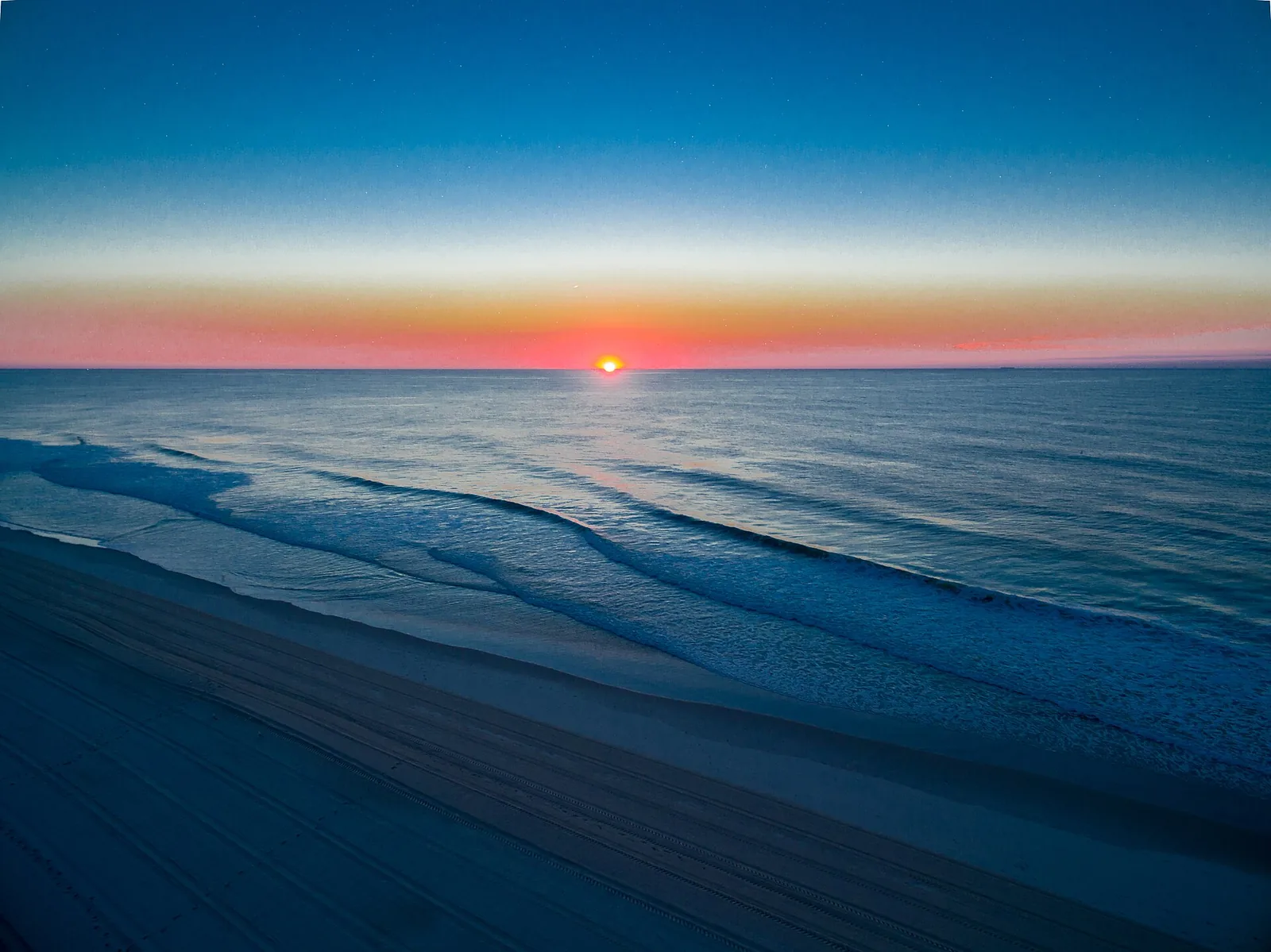 The sun rising over the Atlantic Ocean at Seaside Park, waves washing up a wide, empty beach