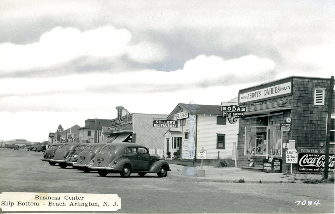 Black-and-white photo of Ship Bottom's early business center, with shingled shops, a sodas sign and 1930s cars parked along the street