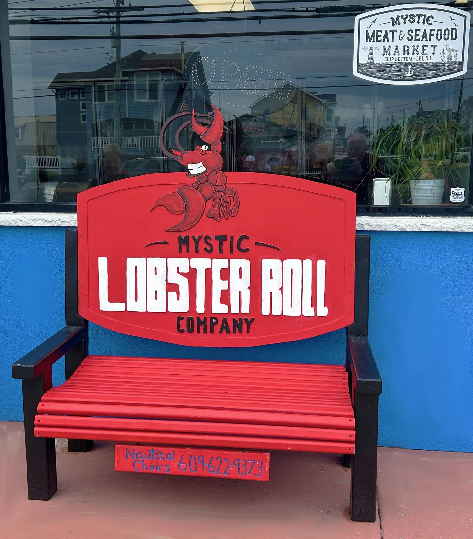 A bright red bench painted with the Mystic Lobster Roll Company logo in front of a blue storefront in Ship Bottom