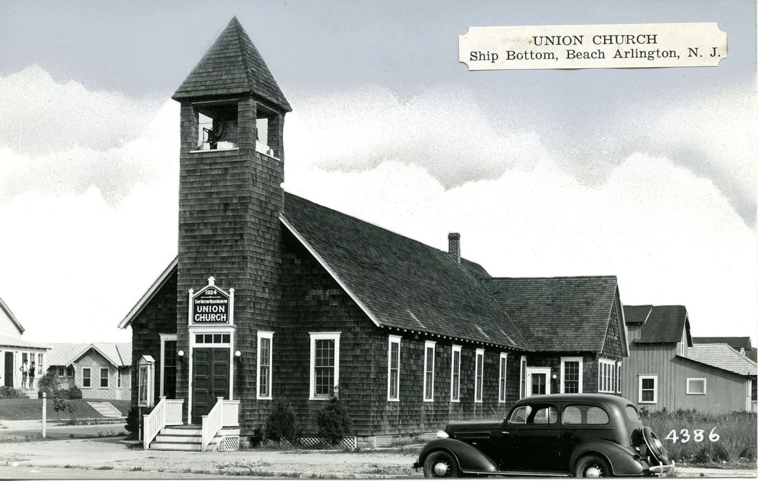 Black-and-white photo of the shingled Union Church with its square bell tower and a 1930s car parked in front