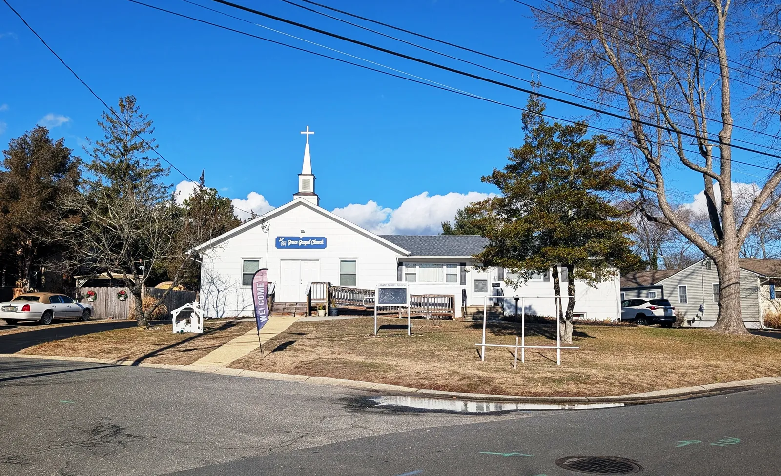 A small white church with a steeple and cross on a sunny winter day, with a front lawn and trees