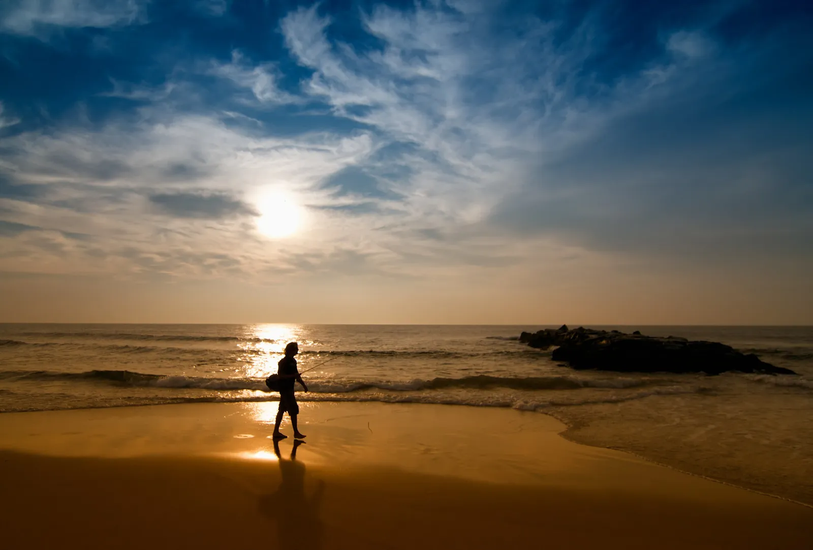 Sunrise over the ocean, with a person silhouetted at the water's edge and a rock jetty offshore